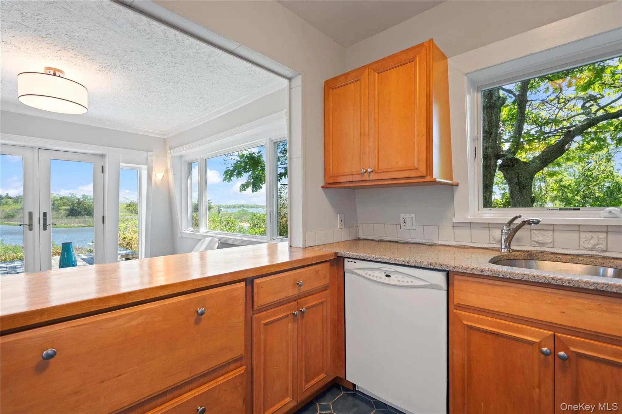Kitchen featuring brown cabinetry, dishwasher, french doors, a textured ceiling, and a water view Kitchen featuring brown cabinetry, dishwasher, french doors, a textured ceiling, and a water view