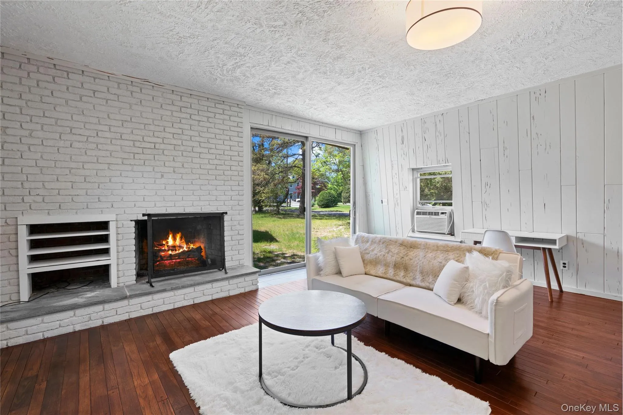 Living room with a brick fireplace, dark wood finished floors, a textured ceiling, and wood walls Living room with a brick fireplace, dark wood finished floors, a textured ceiling, and wood walls