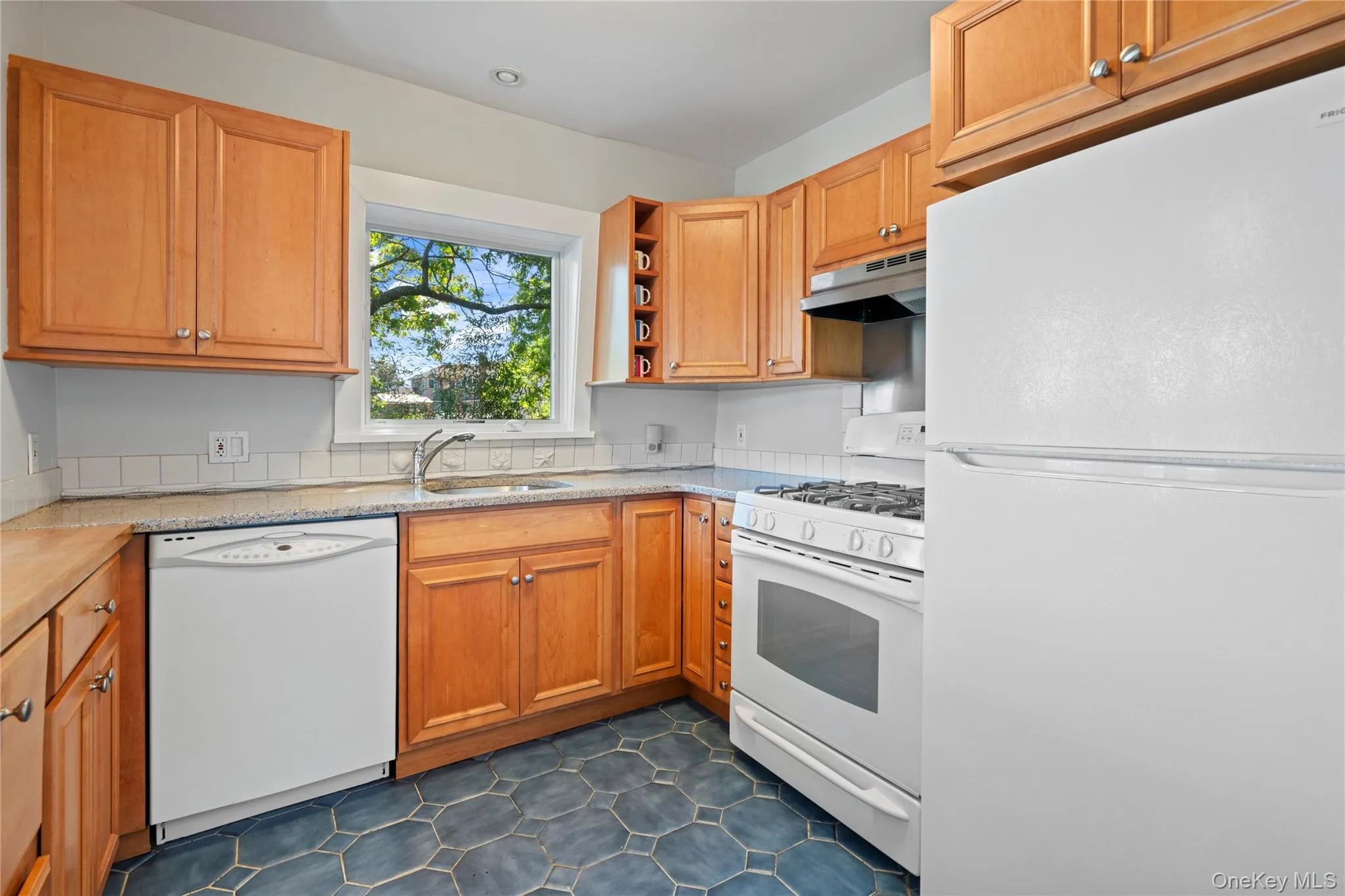Kitchen featuring white appliances, open shelves, under cabinet range hood, brown cabinetry, and dark tile patterned floors Kitchen featuring white appliances, open shelves, under cabinet range hood, brown cabinetry, and dark tile patterned floors