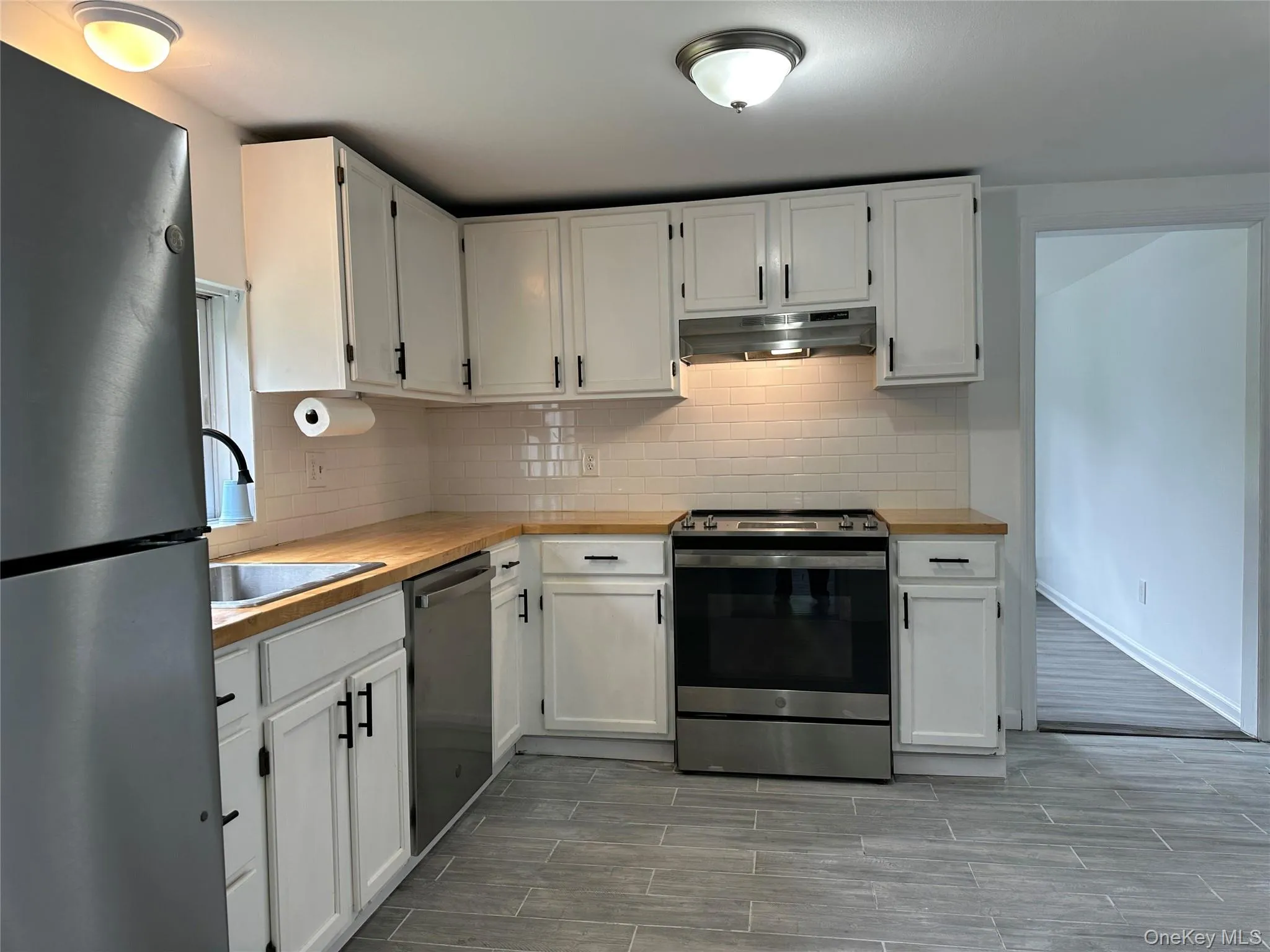 Kitchen featuring appliances with stainless steel finishes, decorative backsplash, white cabinetry, and under cabinet range hood Kitchen featuring appliances with stainless steel finishes, decorative backsplash, white cabinetry, and under cabinet range hood