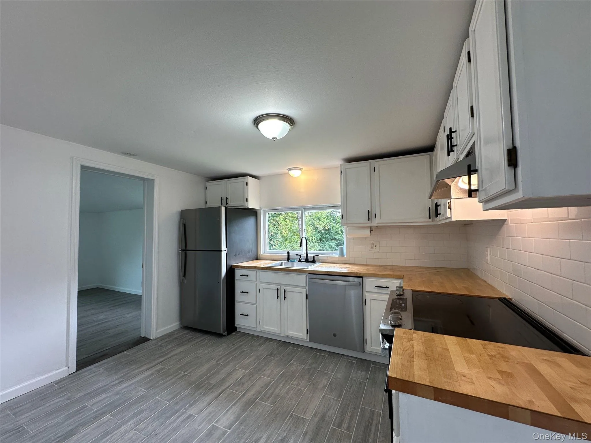 Kitchen featuring wood counters, white cabinetry, appliances with stainless steel finishes, tasteful backsplash, and wood finish floors Kitchen featuring wood counters, white cabinetry, appliances with stainless steel finishes, tasteful backsplash, and wood finish floors