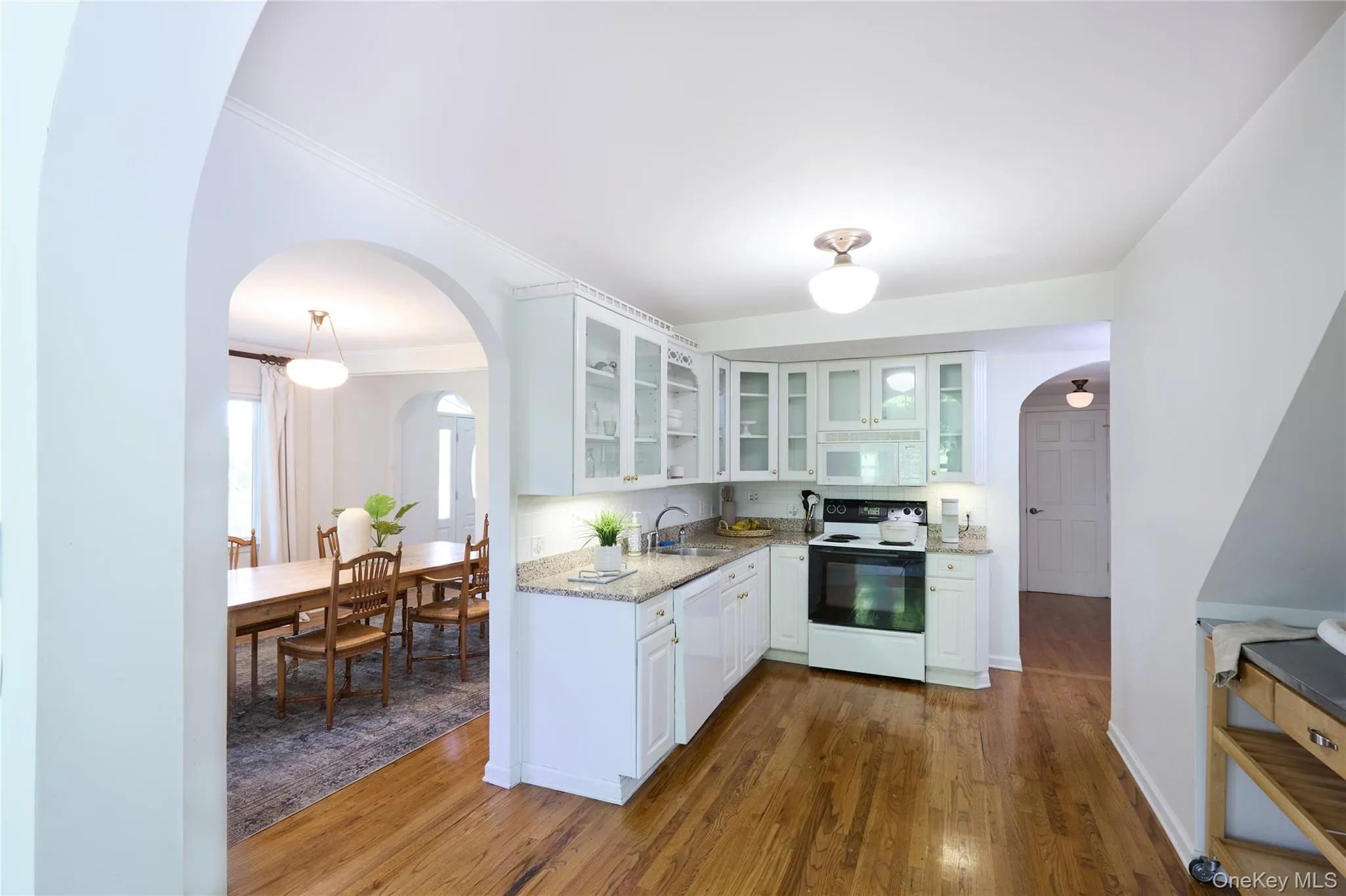 Kitchen with arched walkways, white appliances, white cabinets, light stone countertops, and glass insert cabinets Kitchen with arched walkways, white appliances, white cabinets, light stone countertops, and glass insert cabinets