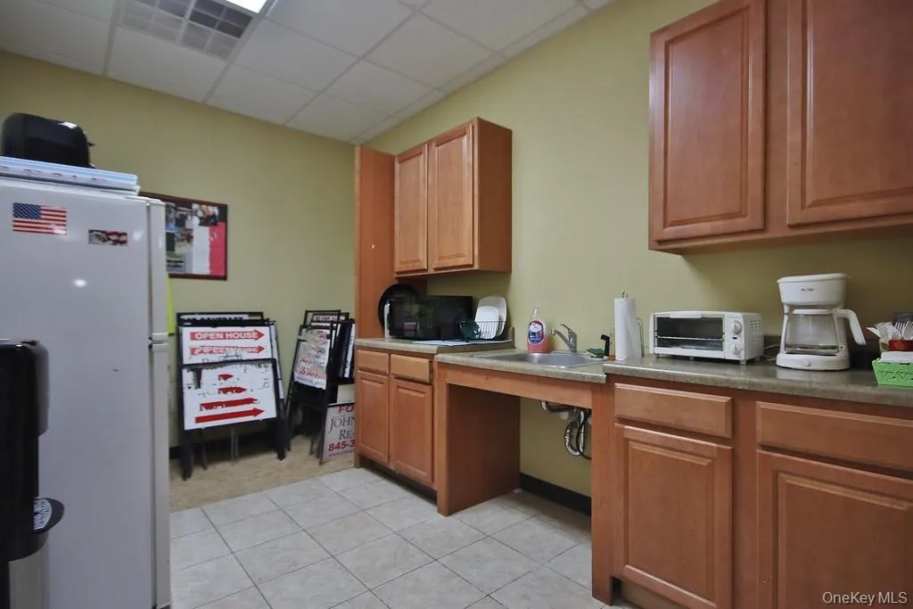 Kitchen featuring white refrigerator, brown cabinets and light tile patterned flooring. Kitchen featuring white refrigerator, brown cabinets and light tile patterned flooring.