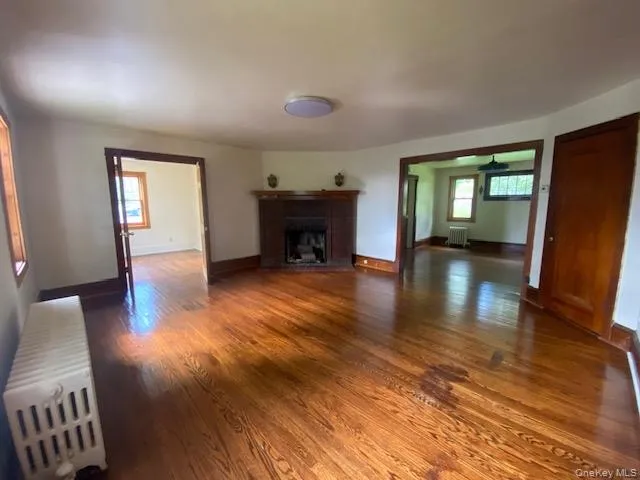 Unfurnished living room featuring radiator, dark wood-type flooring, and a fireplace with flush hearth Unfurnished living room featuring radiator, dark wood-type flooring, and a fireplace with flush hearth