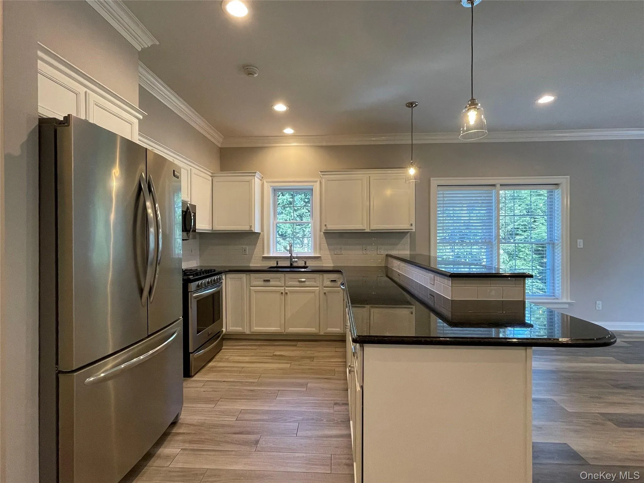 Kitchen with stainless steel appliances, dark stone counters, backsplash, a peninsula, and hanging light fixtures Kitchen with stainless steel appliances, dark stone counters, backsplash, a peninsula, and hanging light fixtures