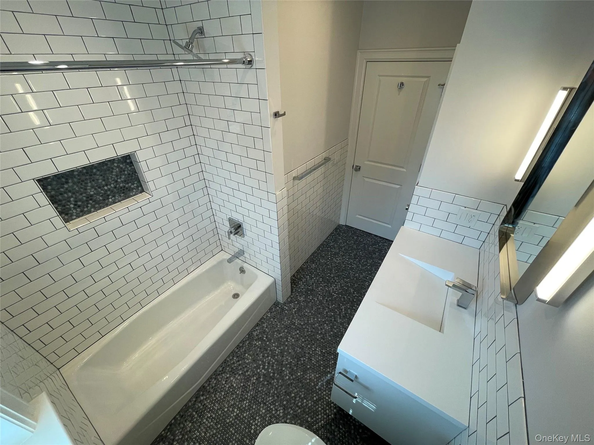 Hall bath featuring tile walls, shower / bath combination, vanity, and wainscoting Hall bath featuring tile walls, shower / bath combination, vanity, and wainscoting