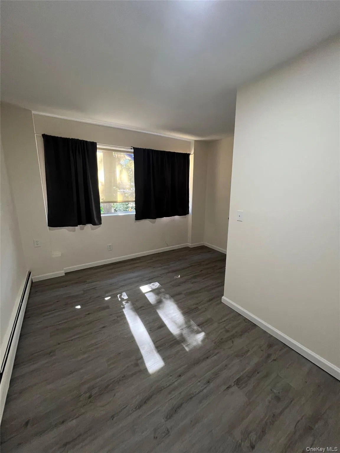 Unfurnished room with a baseboard heating unit and dark wood-style floors Unfurnished room with a baseboard heating unit and dark wood-style floors