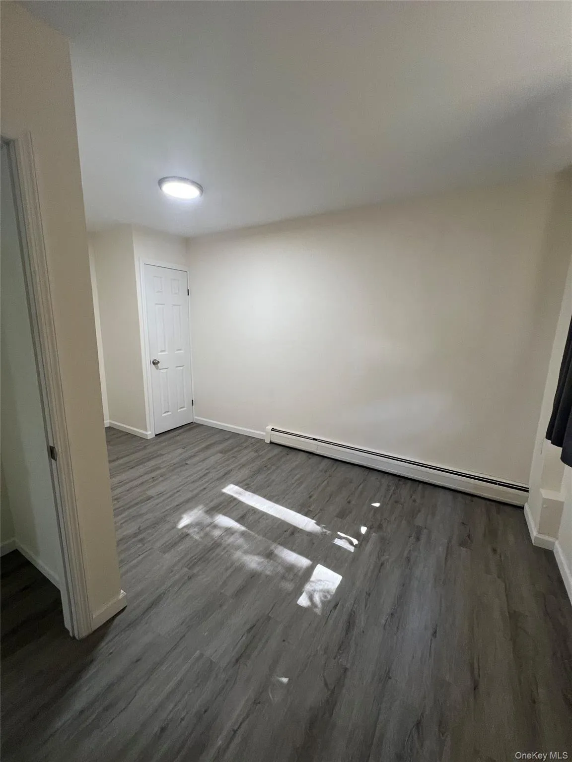 Unfurnished room with baseboard heating and dark wood-style floors Unfurnished room with baseboard heating and dark wood-style floors