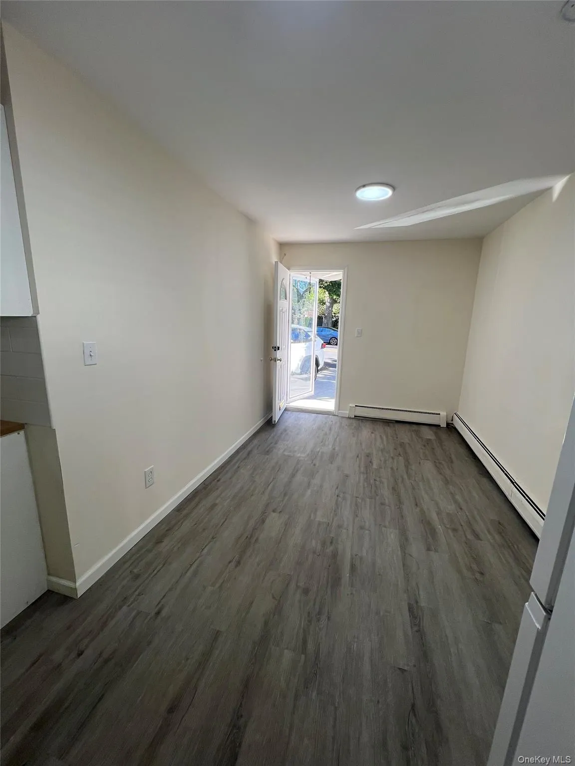 Unfurnished room featuring dark wood-type flooring and baseboard heating Unfurnished room featuring dark wood-type flooring and baseboard heating
