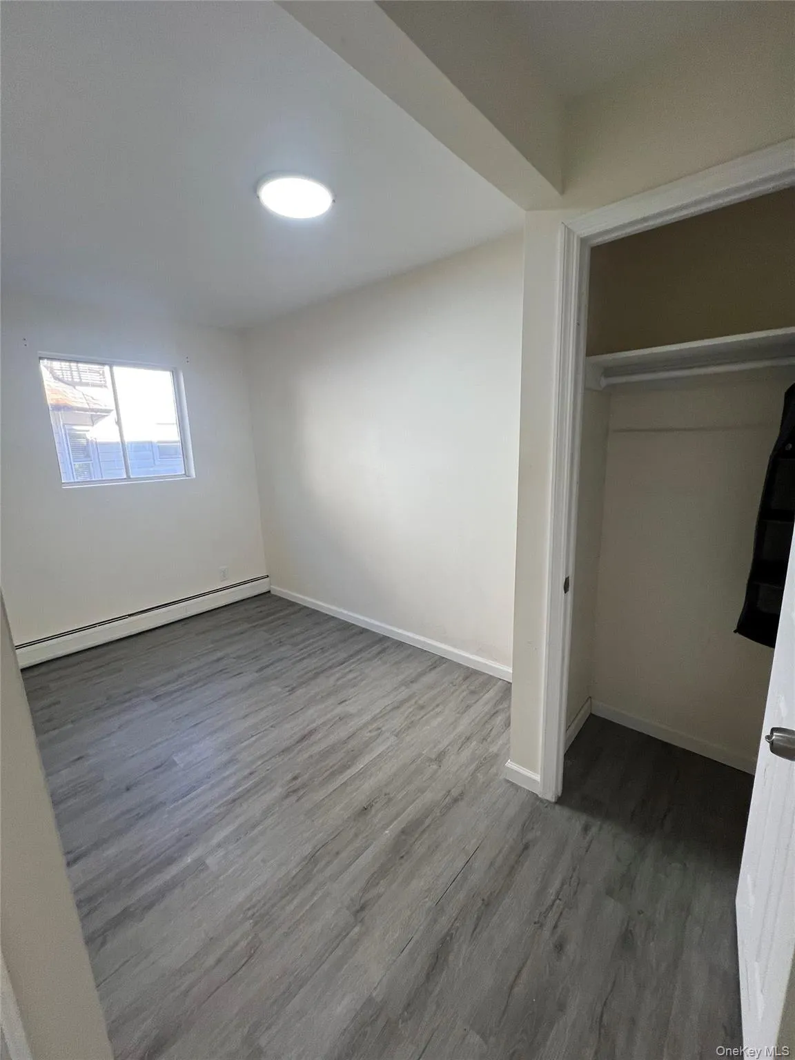 Unfurnished bedroom featuring wood finished floors, a baseboard radiator, and a closet Unfurnished bedroom featuring wood finished floors, a baseboard radiator, and a closet