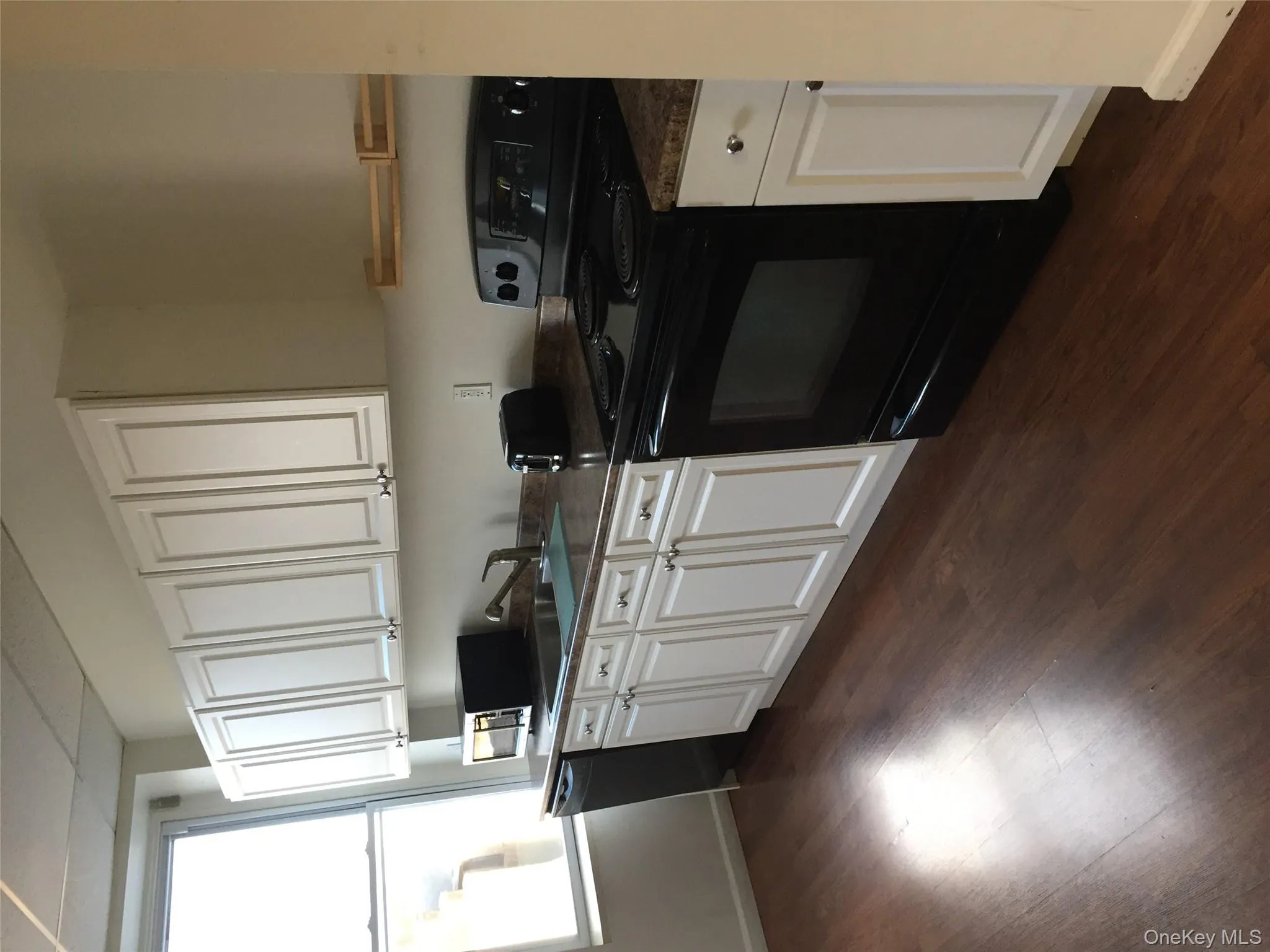 Kitchen featuring range, white cabinetry, dark countertops, dark wood-style floors, and dishwashing machine Kitchen featuring range, white cabinetry, dark countertops, dark wood-style floors, and dishwashing machine