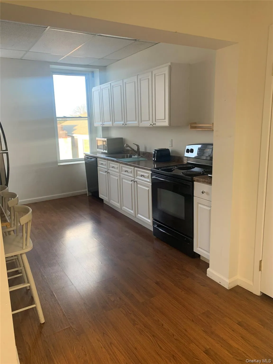 Kitchen with black appliances, white cabinets, dark wood finished floors, dark countertops, and a drop ceiling Kitchen with black appliances, white cabinets, dark wood finished floors, dark countertops, and a drop ceiling