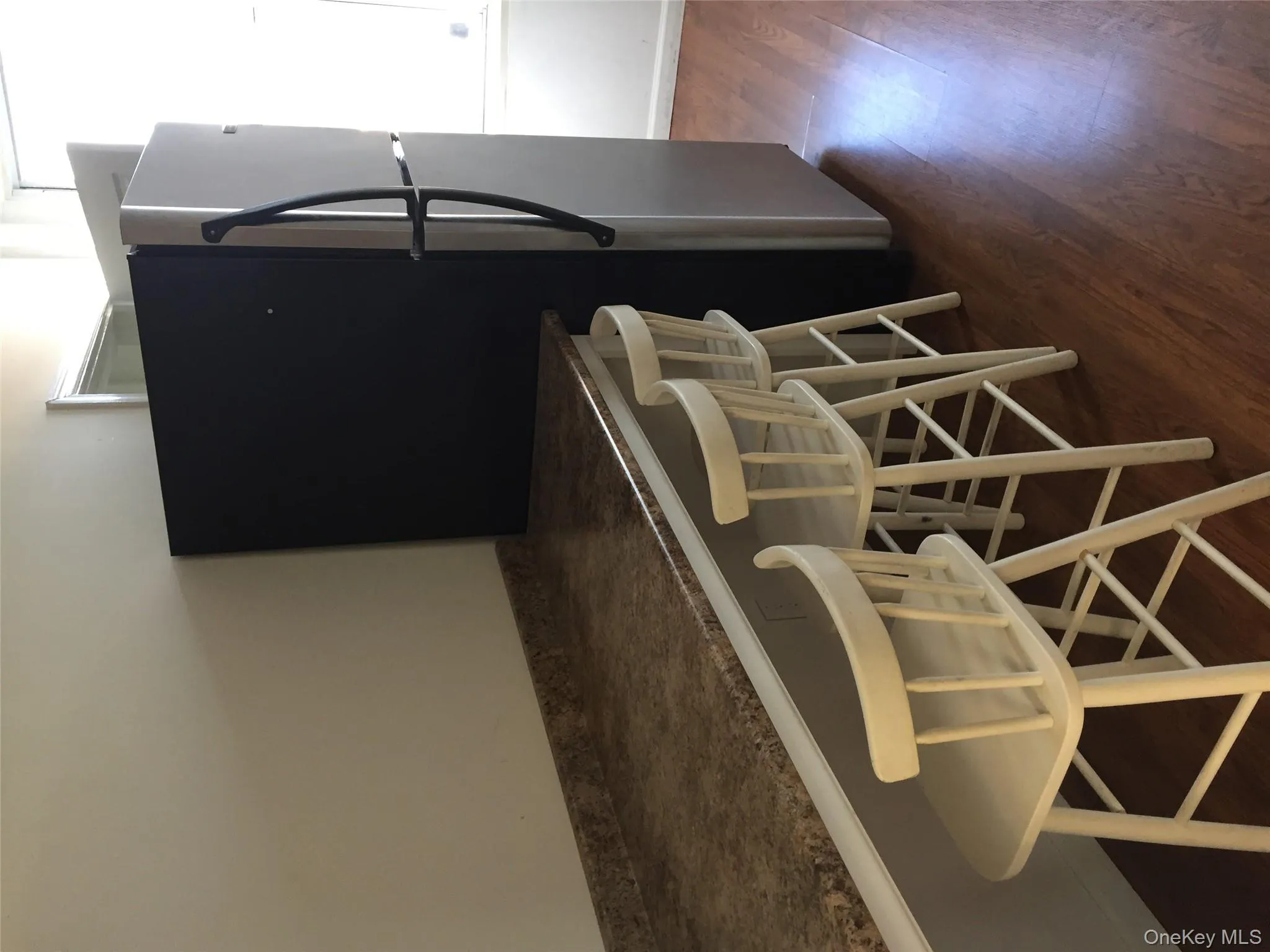Kitchen featuring stainless steel refrigerator, dark wood-style floors, a kitchen breakfast bar, and dark countertops Kitchen featuring stainless steel refrigerator, dark wood-style floors, a kitchen breakfast bar, and dark countertops