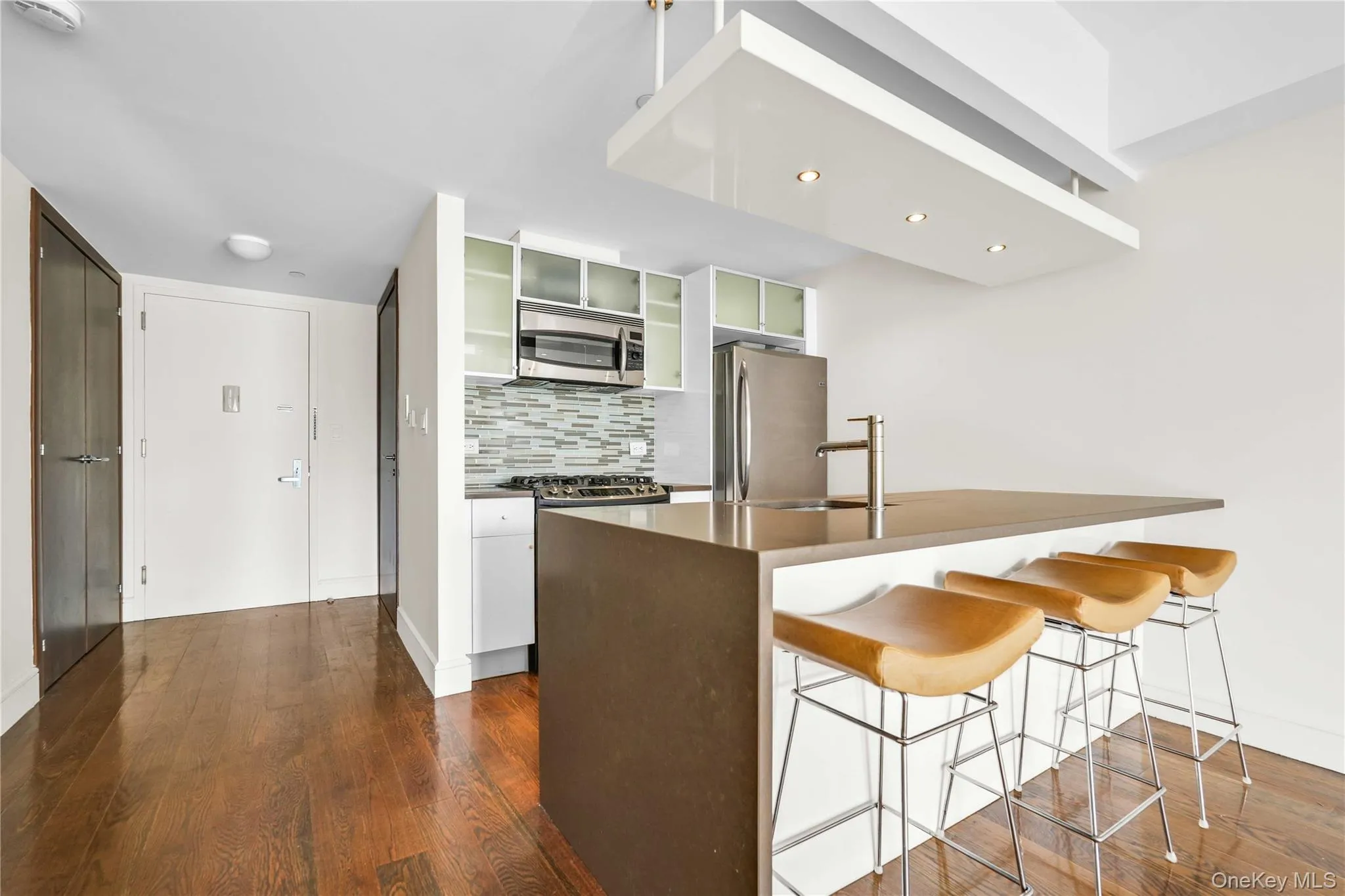 Kitchen with decorative backsplash, appliances with stainless steel finishes, a breakfast bar area, dark wood-style flooring, and glass insert cabinets Kitchen with decorative backsplash, appliances with stainless steel finishes, a breakfast bar area, dark wood-style flooring, and glass insert cabinets