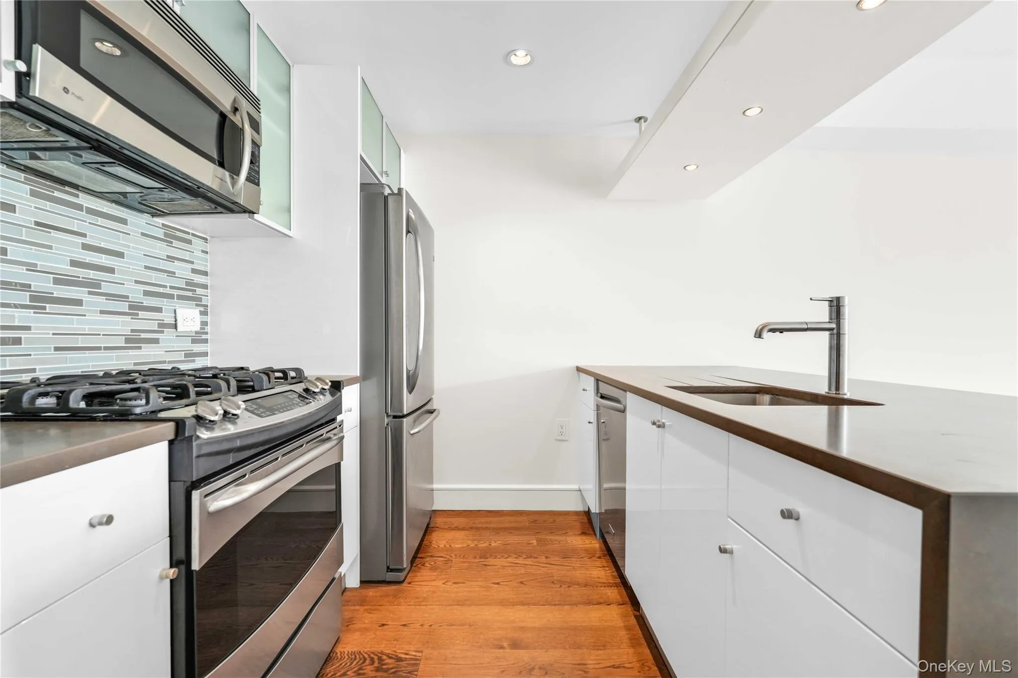 Kitchen featuring appliances with stainless steel finishes, light wood-style flooring, white cabinetry, backsplash, and recessed lighting Kitchen featuring appliances with stainless steel finishes, light wood-style flooring, white cabinetry, backsplash, and recessed lighting
