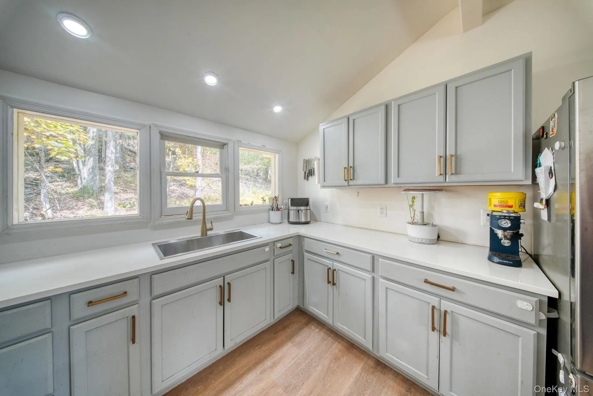 Kitchen featuring gray cabinetry, lofted ceiling, freestanding refrigerator, light wood-style floors, and recessed lighting Kitchen featuring gray cabinetry, lofted ceiling, freestanding refrigerator, light wood-style floors, and recessed lighting