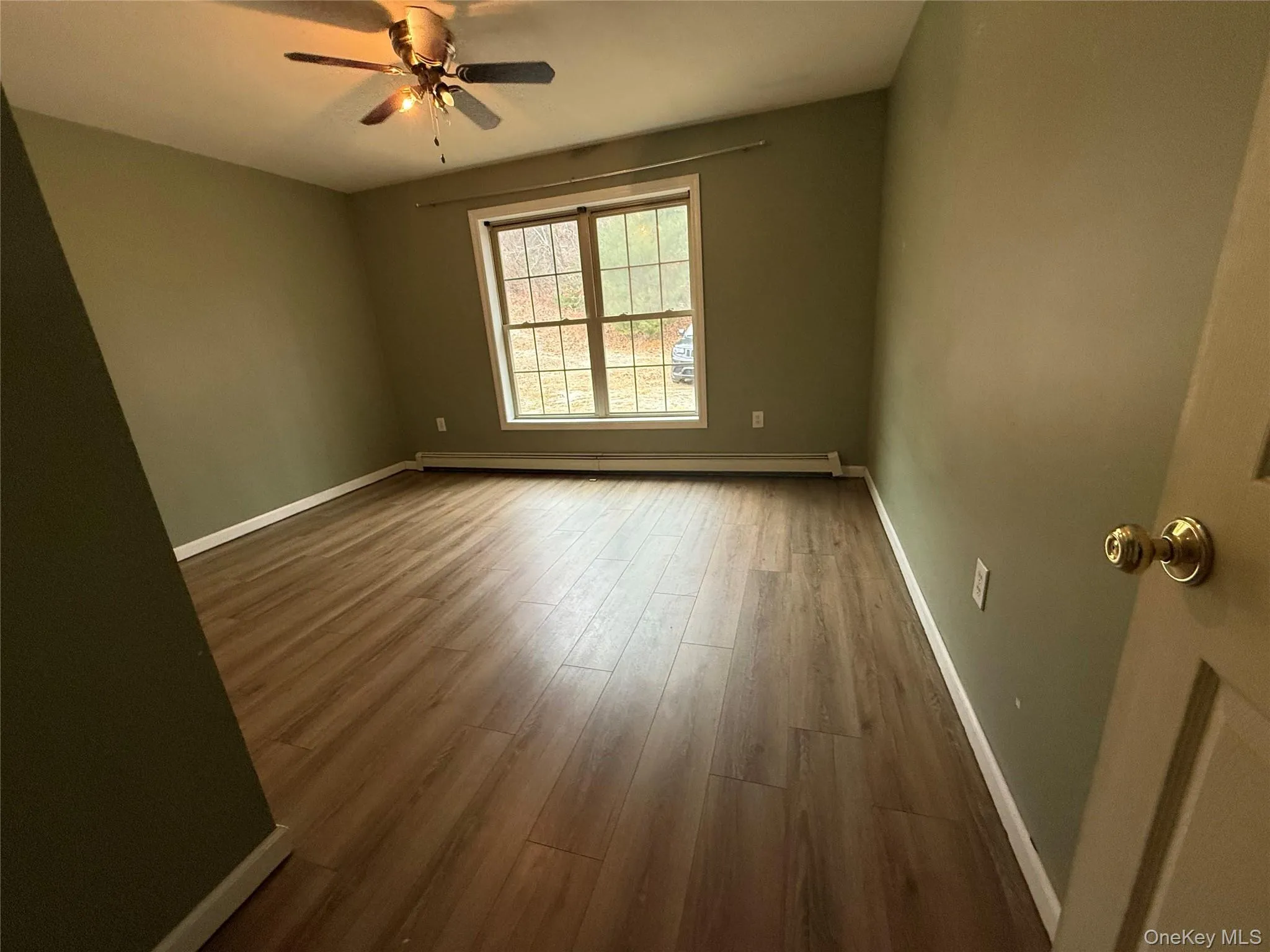Empty room with wood finished floors, a baseboard radiator, and a ceiling fan Empty room with wood finished floors, a baseboard radiator, and a ceiling fan