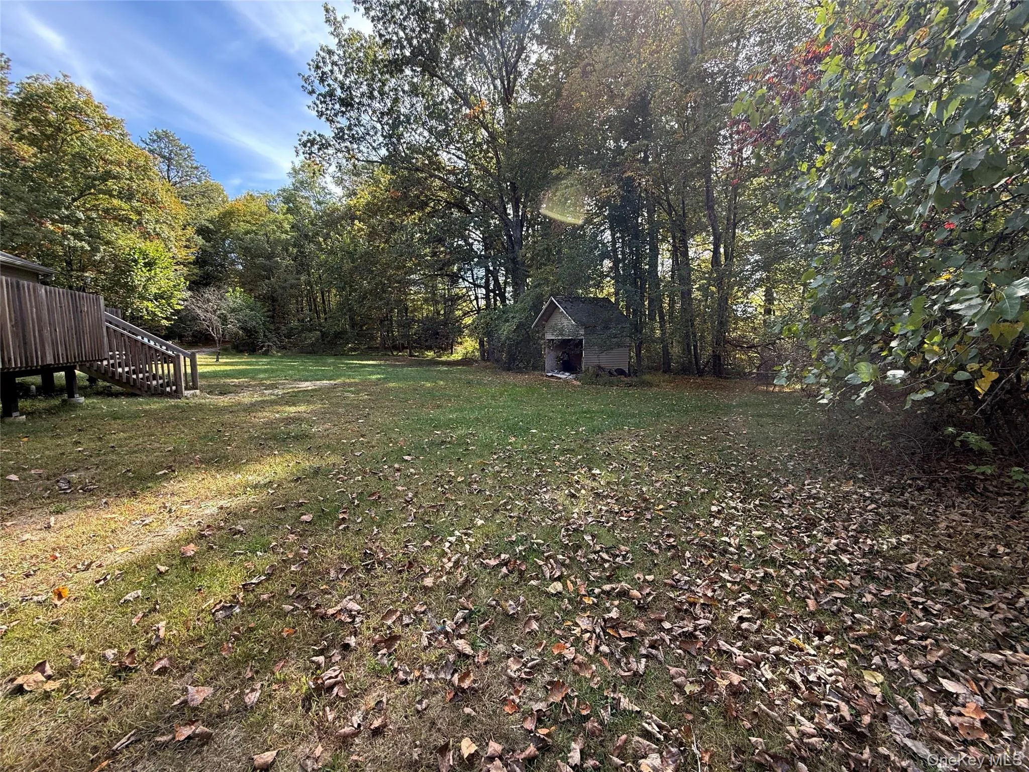 View of green lawn featuring stairs, view of wooded area, an outdoor structure, and a deck View of green lawn featuring stairs, view of wooded area, an outdoor structure, and a deck