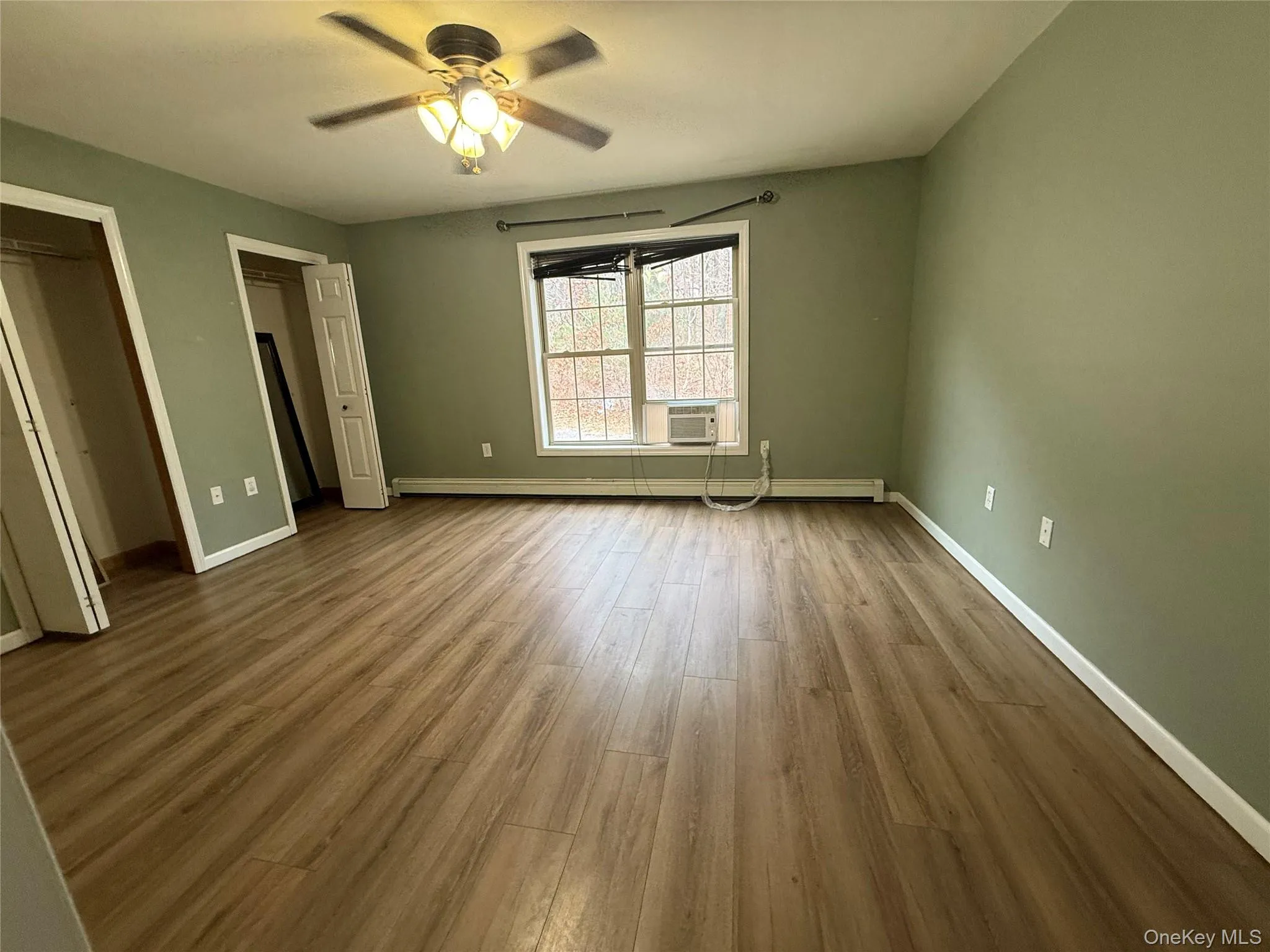 Unfurnished bedroom featuring wood finished floors, ceiling fan, and baseboard heating Unfurnished bedroom featuring wood finished floors, ceiling fan, and baseboard heating