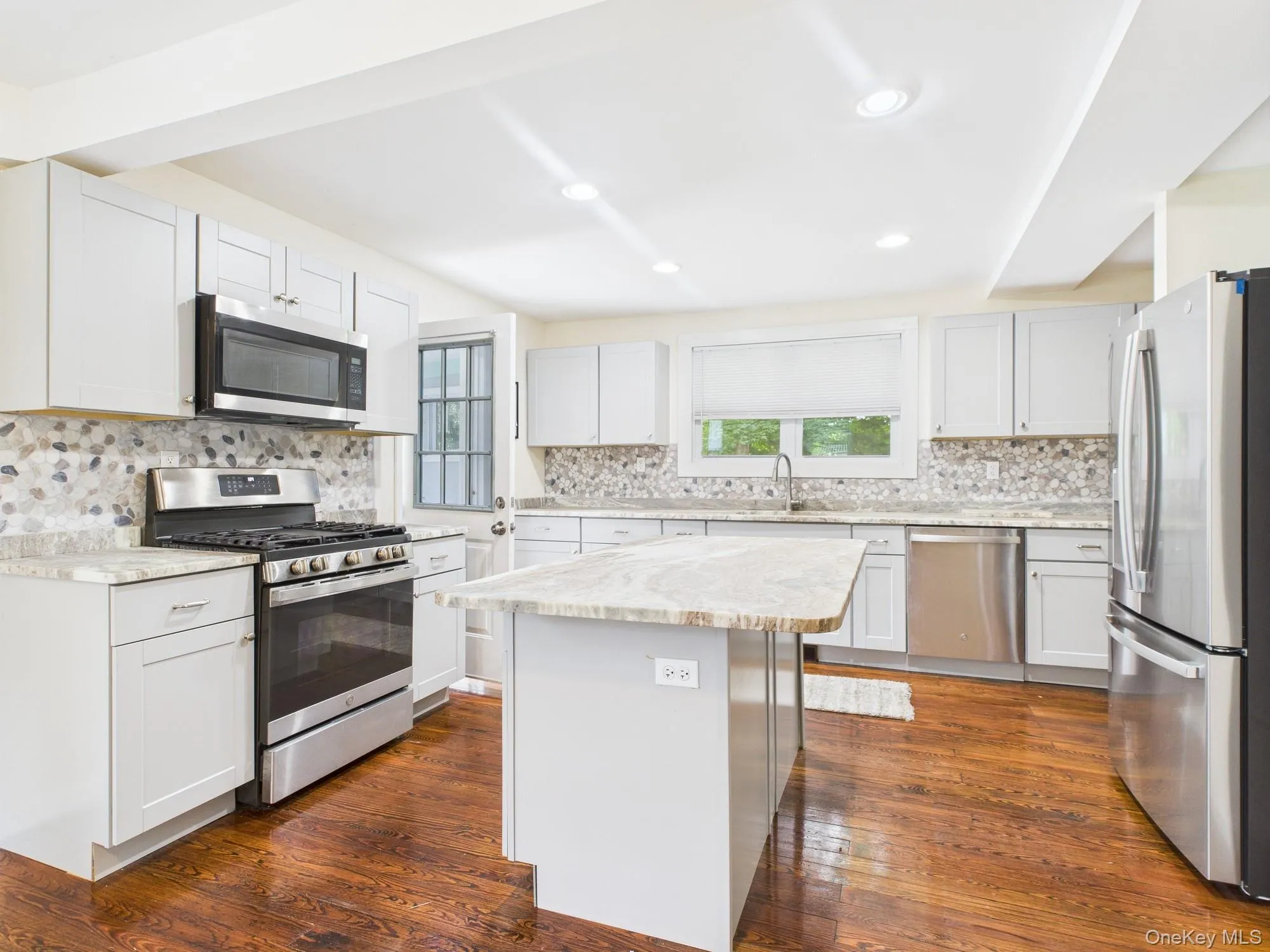 Kitchen with stainless steel appliances, tasteful backsplash, a center island, dark wood-type flooring, and recessed lighting Kitchen with stainless steel appliances, tasteful backsplash, a center island, dark wood-type flooring, and recessed lighting