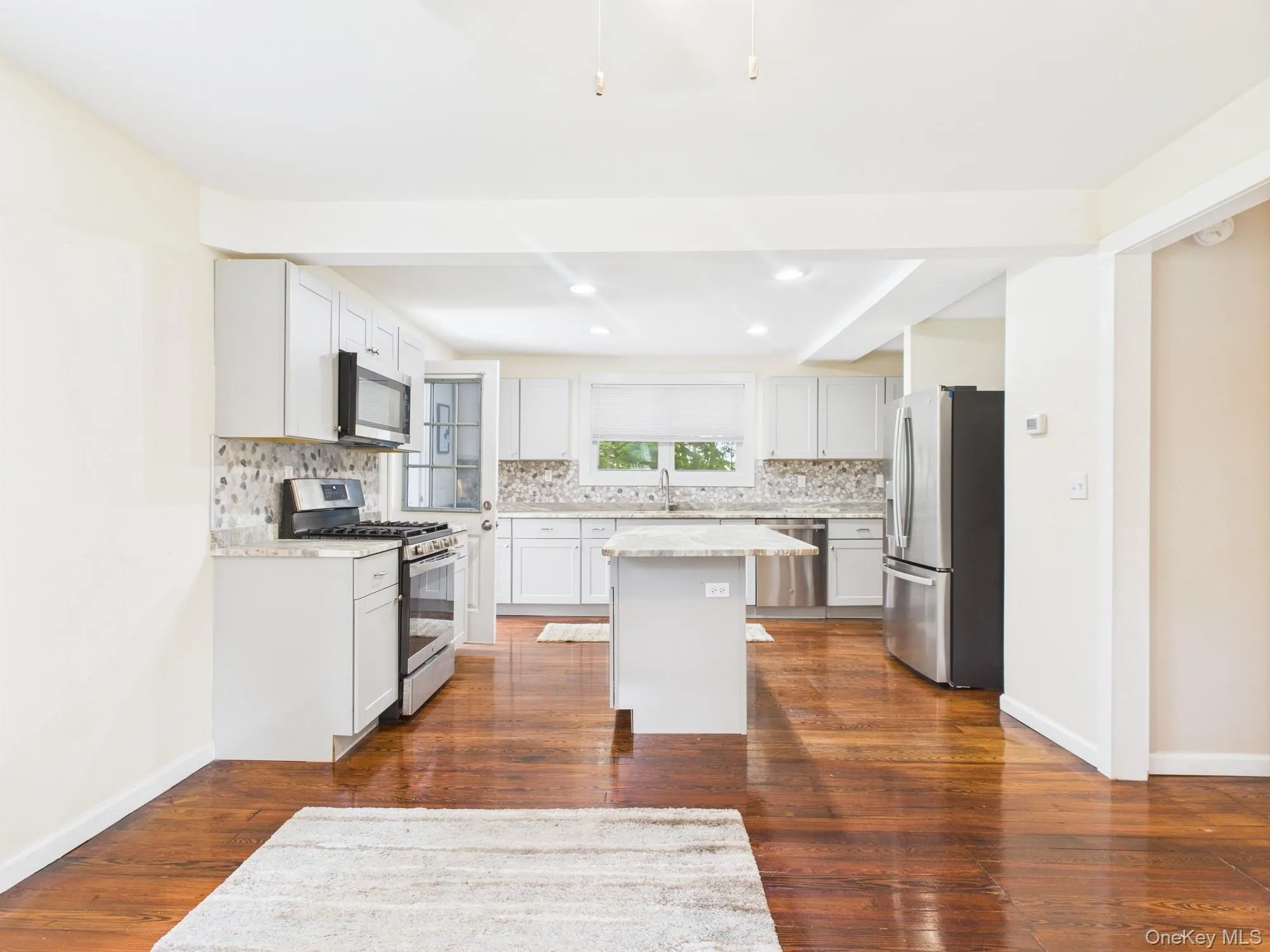 Kitchen with appliances with stainless steel finishes, tasteful backsplash, a kitchen island, dark wood finished floors, and recessed lighting Kitchen with appliances with stainless steel finishes, tasteful backsplash, a kitchen island, dark wood finished floors, and recessed lighting