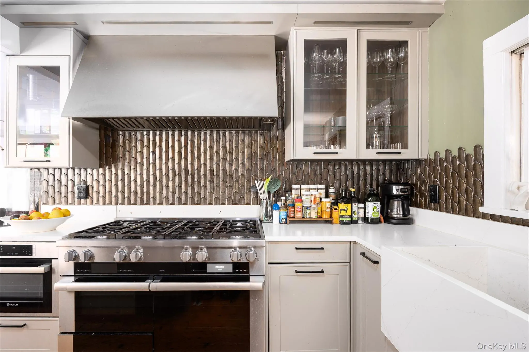 Kitchen with range with two ovens, extractor fan, glass insert cabinets, decorative backsplash, and white cabinetry Kitchen with range with two ovens, extractor fan, glass insert cabinets, decorative backsplash, and white cabinetry