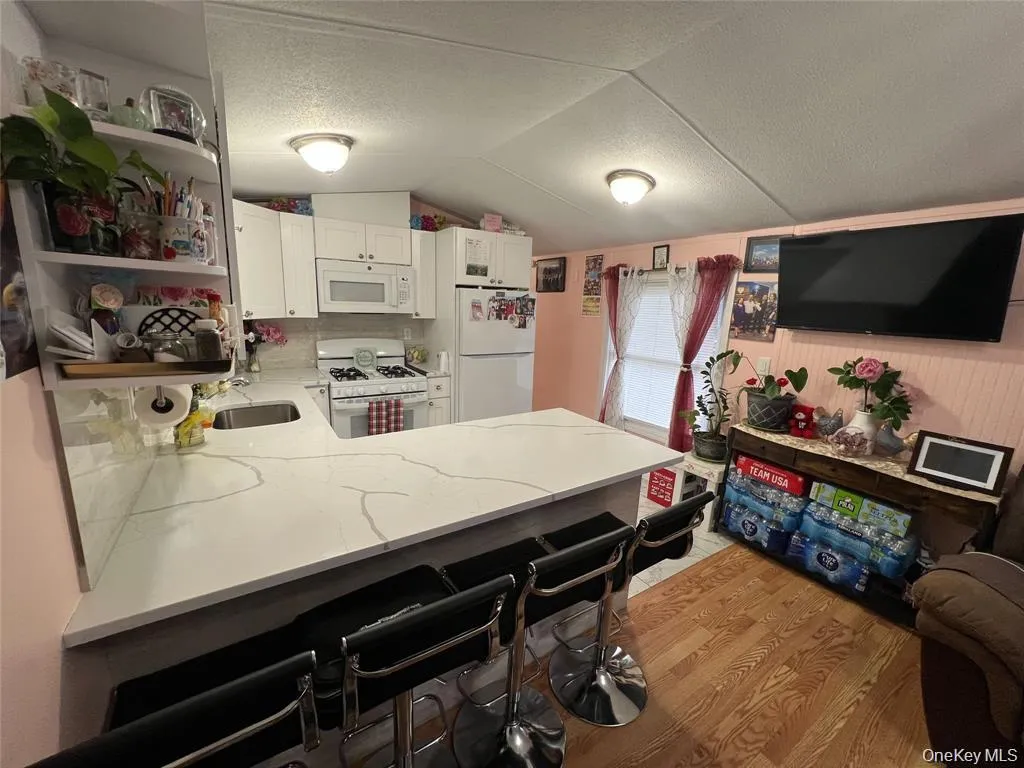 Kitchen featuring open shelves, a kitchen bar, white appliances, a peninsula, and white cabinets Kitchen featuring open shelves, a kitchen bar, white appliances, a peninsula, and white cabinets