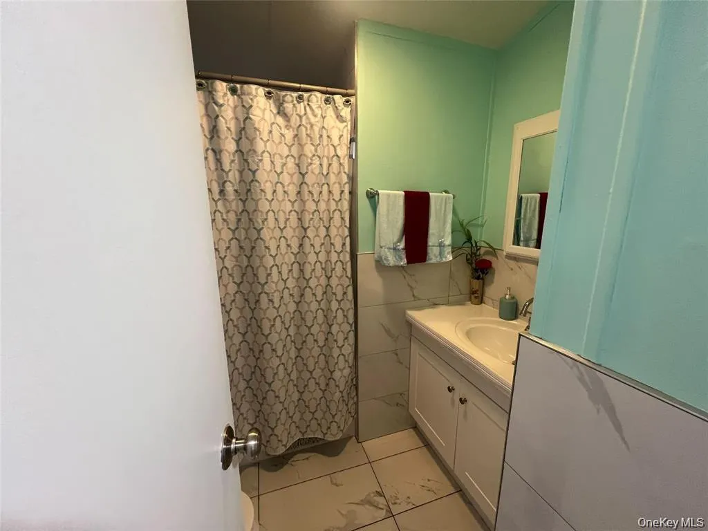 Full bathroom featuring vanity, tile walls, curtained shower, and light tile patterned flooring Full bathroom featuring vanity, tile walls, curtained shower, and light tile patterned flooring