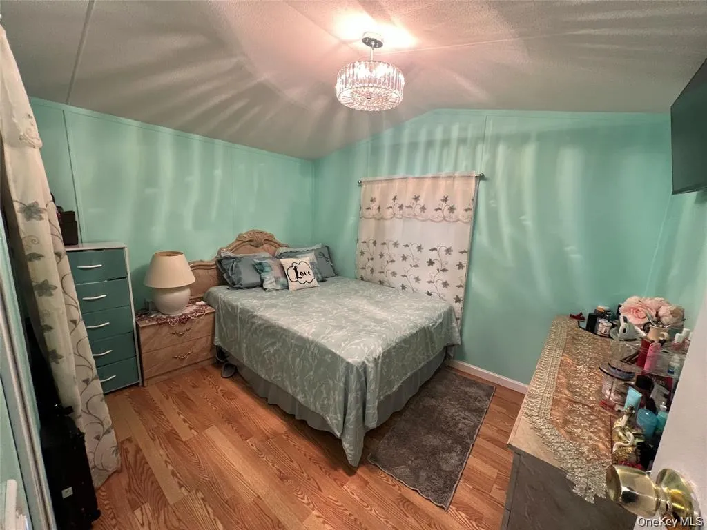 Bedroom featuring vaulted ceiling, wood finished floors, a chandelier, and a textured ceiling Bedroom featuring vaulted ceiling, wood finished floors, a chandelier, and a textured ceiling