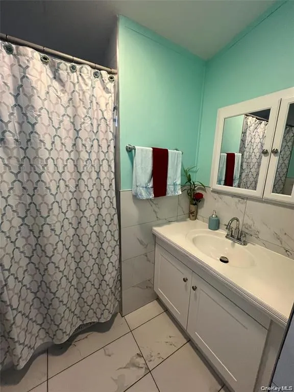 Bathroom featuring vanity, tile walls, and a shower with shower curtain Bathroom featuring vanity, tile walls, and a shower with shower curtain