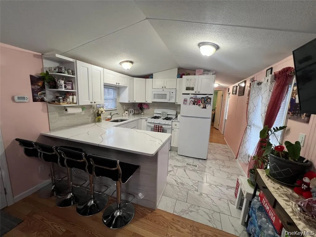 Kitchen with white cabinets, white appliances, open shelves, a breakfast bar, and vaulted ceiling Kitchen with white cabinets, white appliances, open shelves, a breakfast bar, and vaulted ceiling