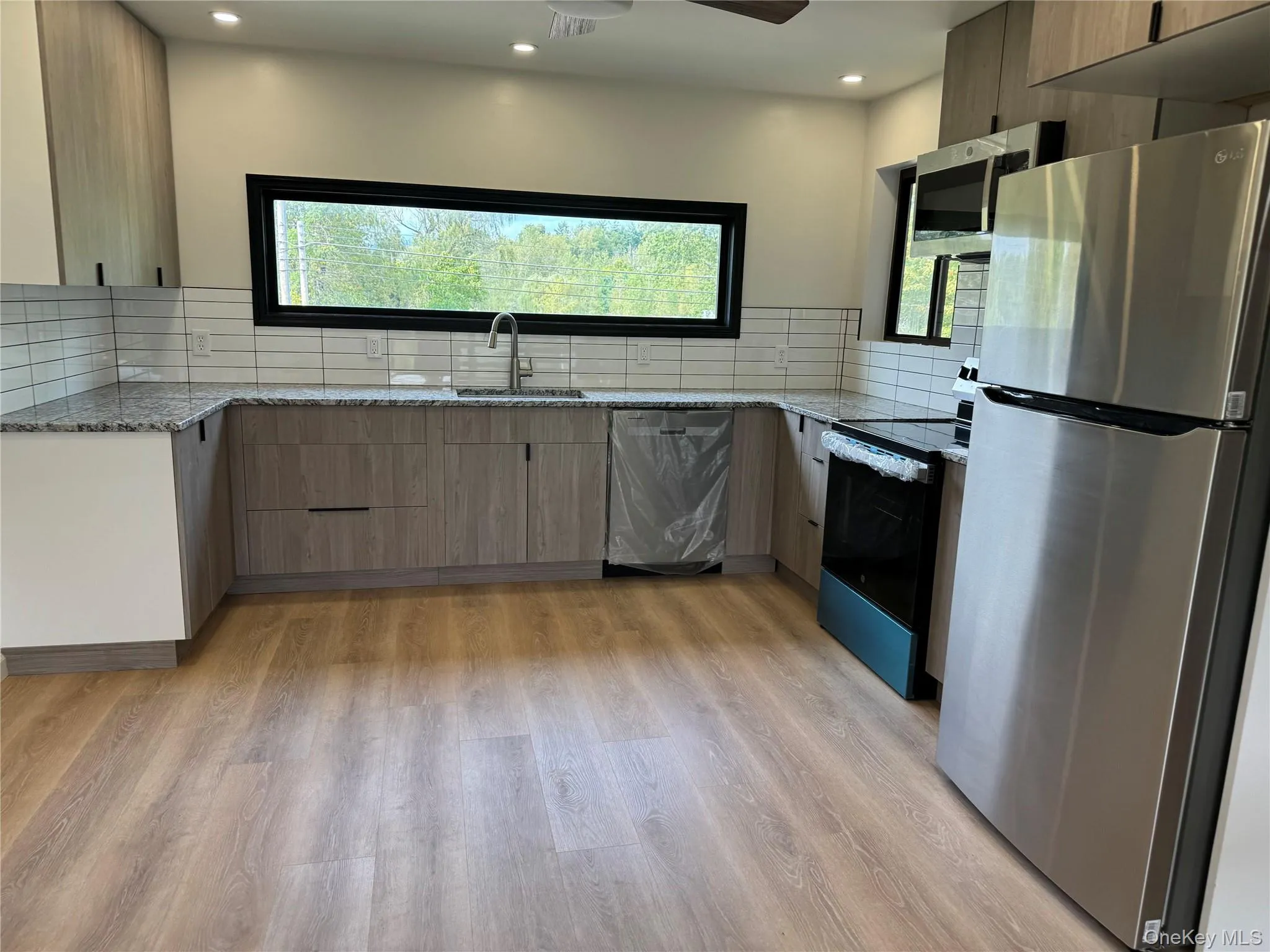 Kitchen with light stone counters, appliances with stainless steel finishes, light wood-type flooring, backsplash, and recessed lighting Kitchen with light stone counters, appliances with stainless steel finishes, light wood-type flooring, backsplash, and recessed lighting