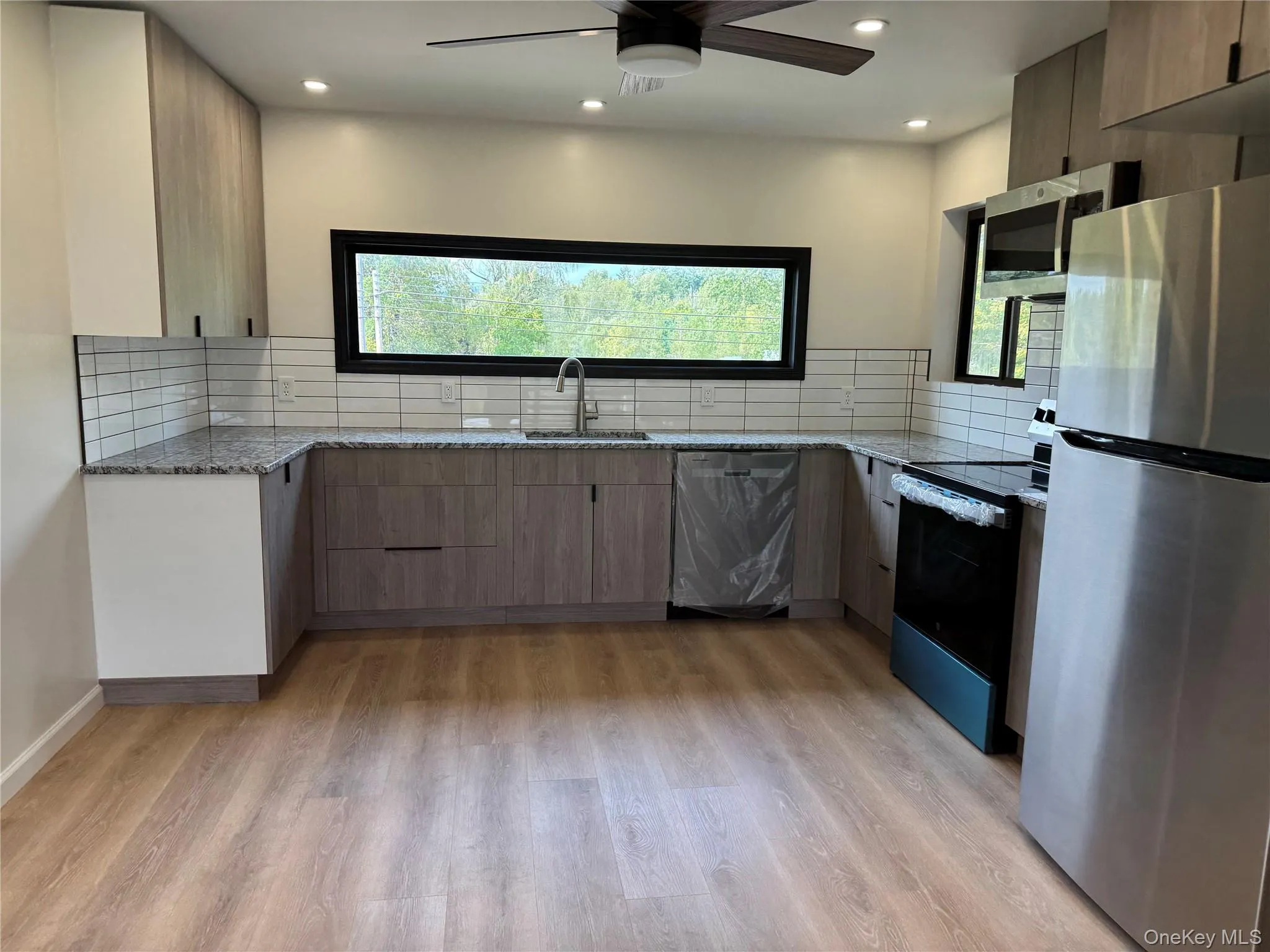 Kitchen with light stone countertops, appliances with stainless steel finishes, decorative backsplash, light wood-style flooring, and recessed lighting Kitchen with light stone countertops, appliances with stainless steel finishes, decorative backsplash, light wood-style flooring, and recessed lighting