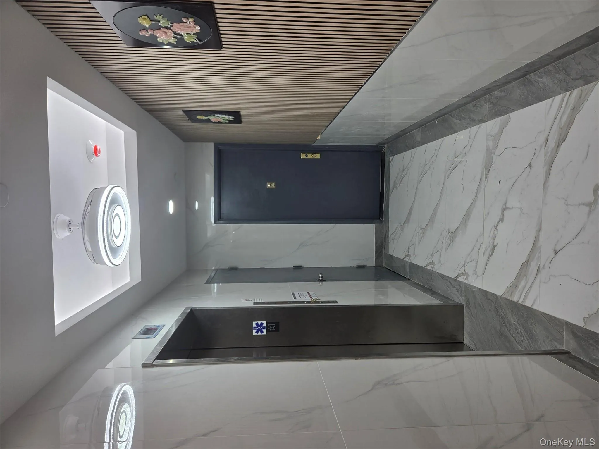 Hallway with light marble finish flooring, elevator, and a raised ceiling Hallway with light marble finish flooring, elevator, and a raised ceiling
