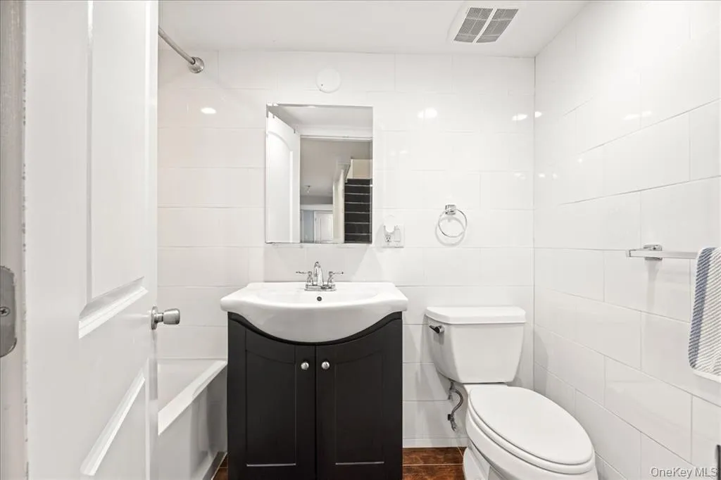 Bathroom featuring tile walls, vanity, and dark tile patterned flooring Bathroom featuring tile walls, vanity, and dark tile patterned flooring