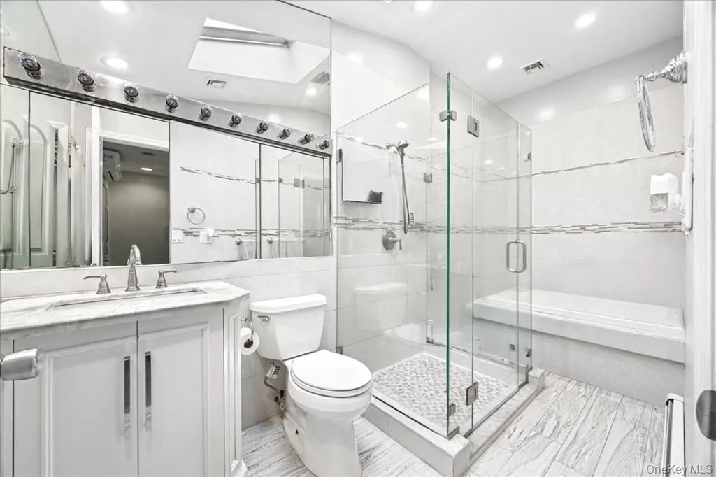 Bathroom featuring a skylight, tile walls, a stall shower, vanity, and recessed lighting Bathroom featuring a skylight, tile walls, a stall shower, vanity, and recessed lighting