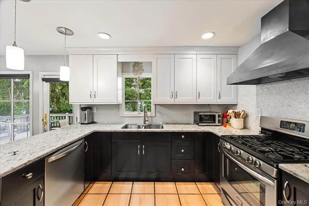 Kitchen featuring appliances with stainless steel finishes, wall chimney range hood, dark cabinetry, white cabinetry, and light stone countertops Kitchen featuring appliances with stainless steel finishes, wall chimney range hood, dark cabinetry, white cabinetry, and light stone countertops