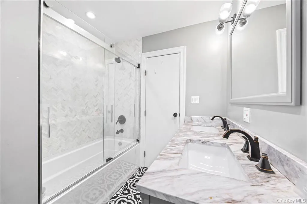 Full bath featuring shower / bath combination with glass door and double vanity Full bath featuring shower / bath combination with glass door and double vanity