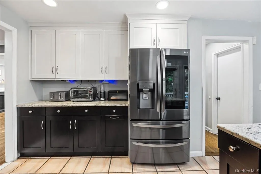 Kitchen with stainless steel refrigerator with ice dispenser, dark cabinets, white cabinetry, light stone countertops, and recessed lighting Kitchen with stainless steel refrigerator with ice dispenser, dark cabinets, white cabinetry, light stone countertops, and recessed lighting