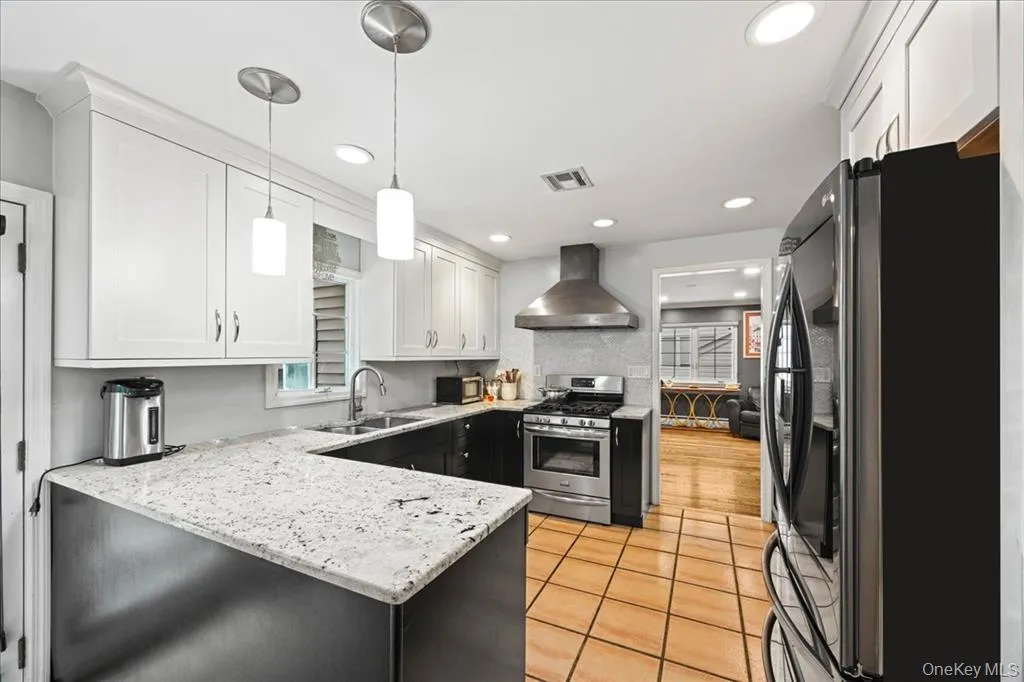 Kitchen featuring appliances with stainless steel finishes, light stone countertops, wall chimney exhaust hood, pendant lighting, and light tile patterned floors Kitchen featuring appliances with stainless steel finishes, light stone countertops, wall chimney exhaust hood, pendant lighting, and light tile patterned floors