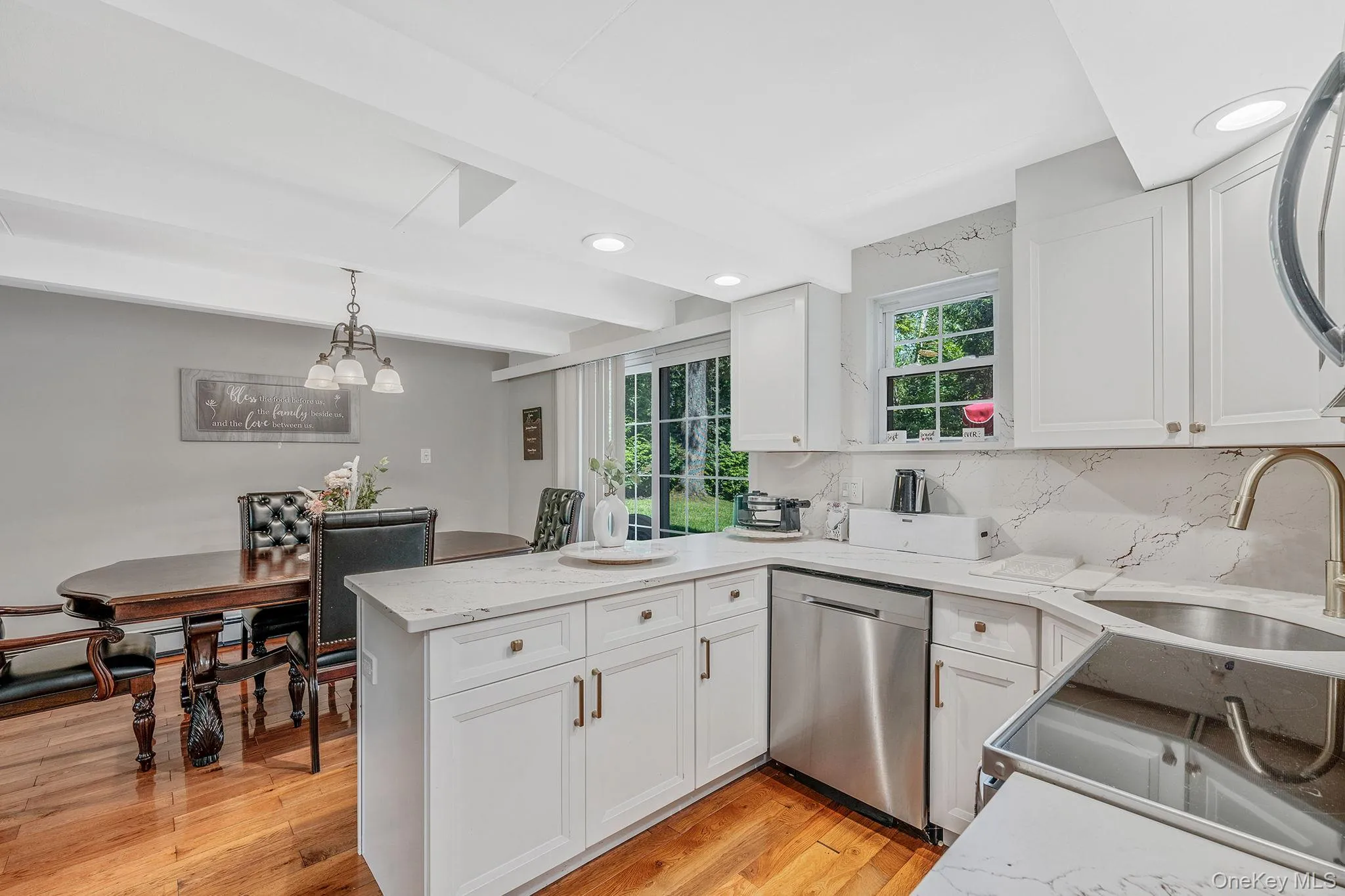Kitchen with decorative light fixtures, decorative backsplash, a peninsula, stainless steel dishwasher, and white cabinets Kitchen with decorative light fixtures, decorative backsplash, a peninsula, stainless steel dishwasher, and white cabinets
