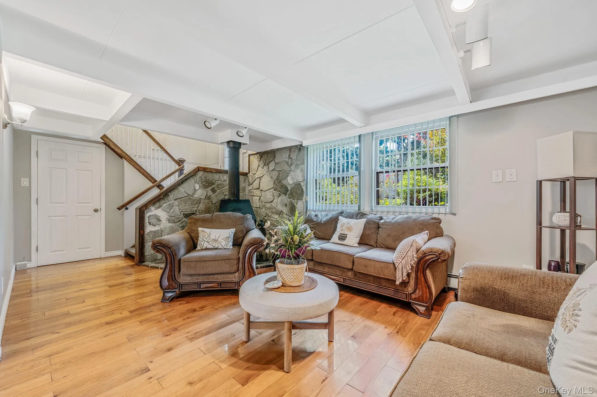 Living area featuring a wood stove, beamed ceiling, stairway, and light wood-style flooring Living area featuring a wood stove, beamed ceiling, stairway, and light wood-style flooring