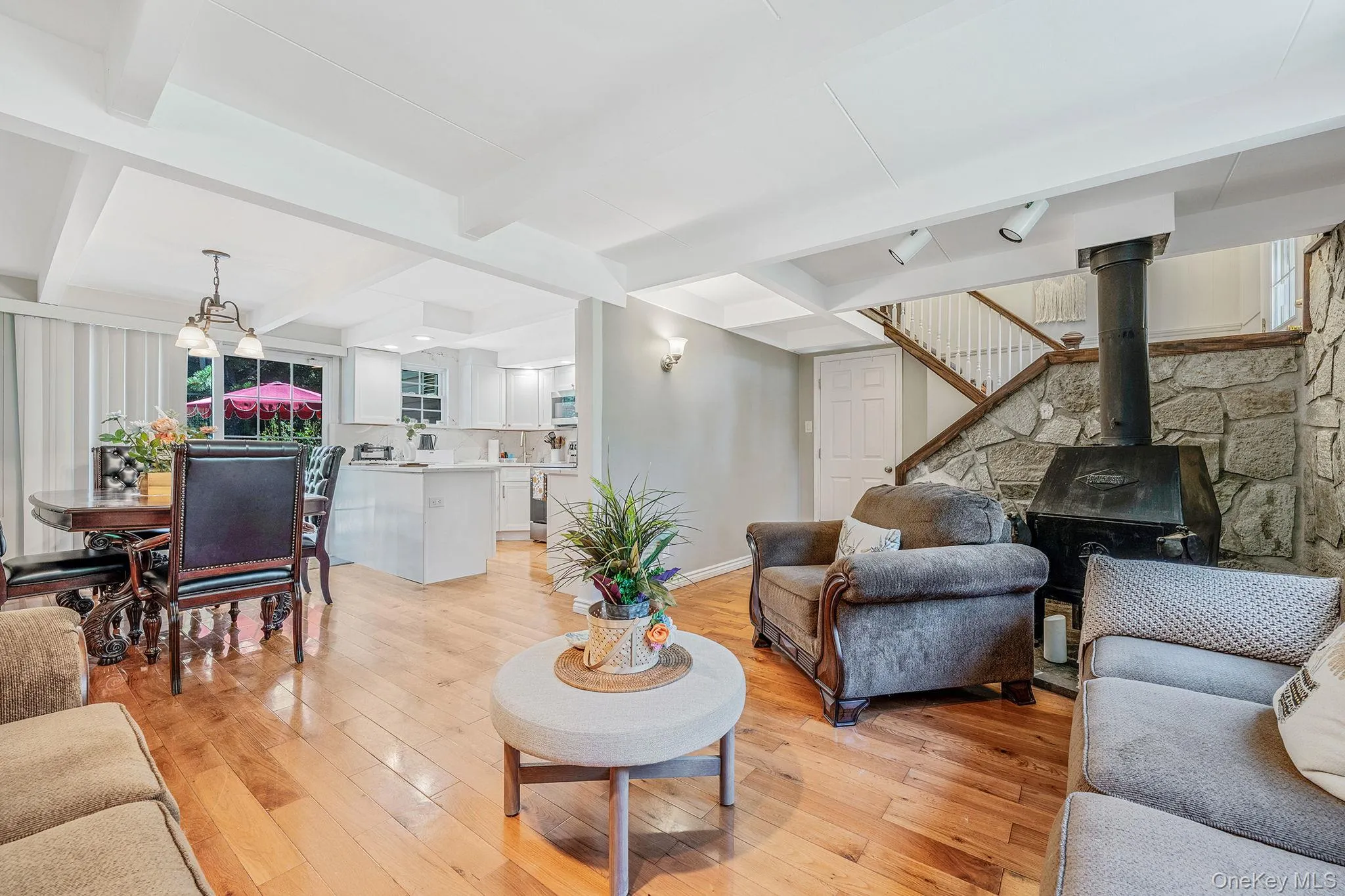 Living room with beamed ceiling, a wood stove, light wood-type flooring, stairway, and a chandelier Living room with beamed ceiling, a wood stove, light wood-type flooring, stairway, and a chandelier