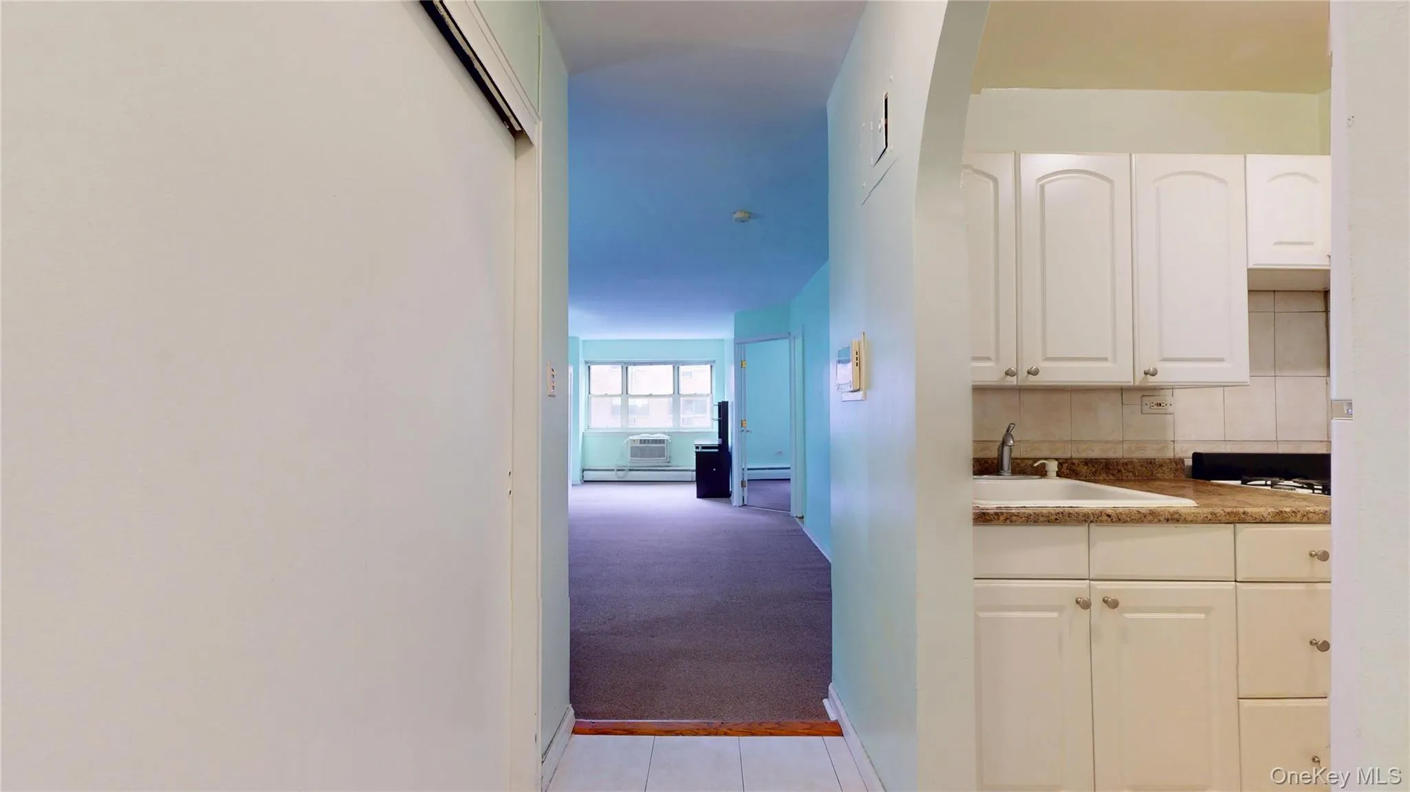 Corridor with light carpet, a baseboard heating unit, a wall mounted AC, and light tile patterned floors Corridor with light carpet, a baseboard heating unit, a wall mounted AC, and light tile patterned floors
