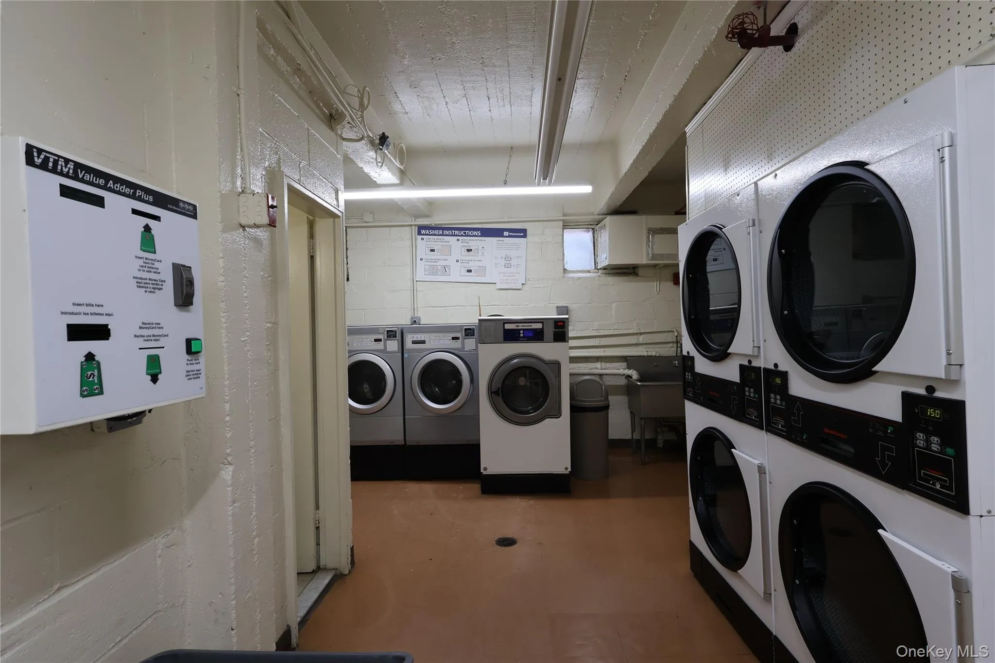 Shared laundry with stacked washer / dryer, water heater, and concrete block wall Shared laundry with stacked washer / dryer, water heater, and concrete block wall