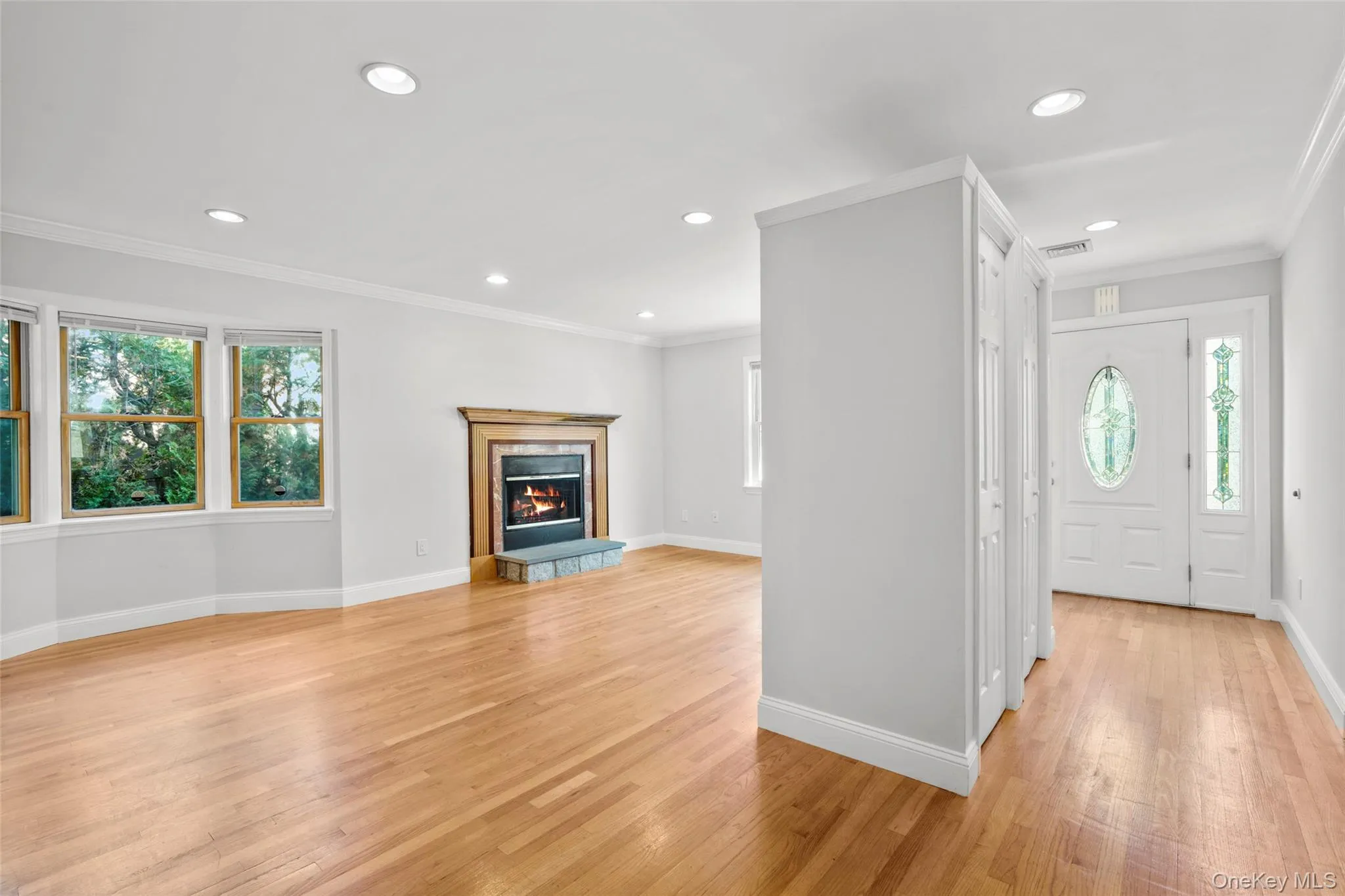 Foyer entrance with crown molding, coat closet, light wood finished floors, recessed lighting, and a fireplace Foyer entrance with crown molding, coat closet, light wood finished floors, recessed lighting, and a fireplace