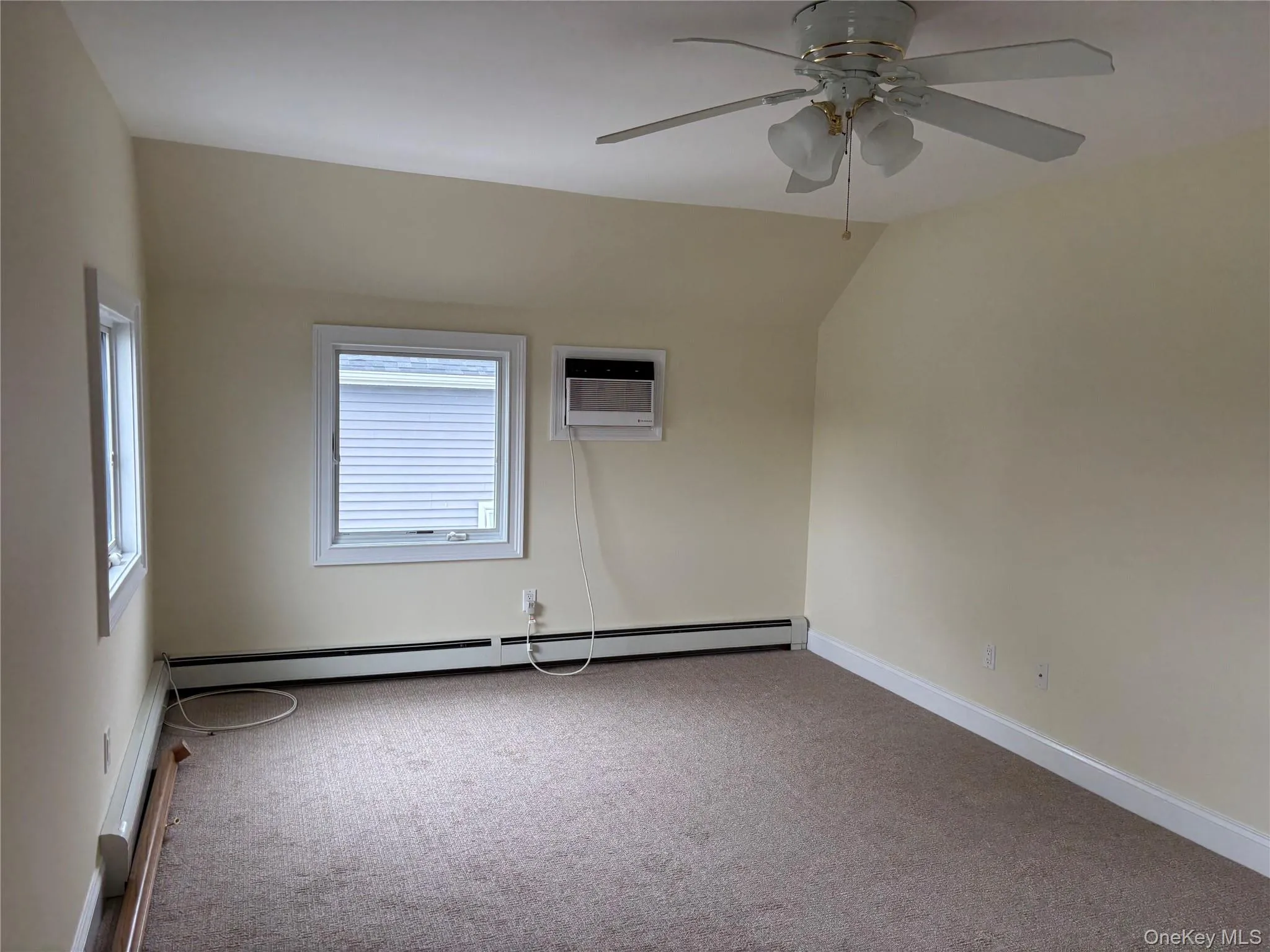 Empty room with carpet floors, a baseboard radiator, baseboard heating, an AC wall unit, and lofted ceiling Empty room with carpet floors, a baseboard radiator, baseboard heating, an AC wall unit, and lofted ceiling