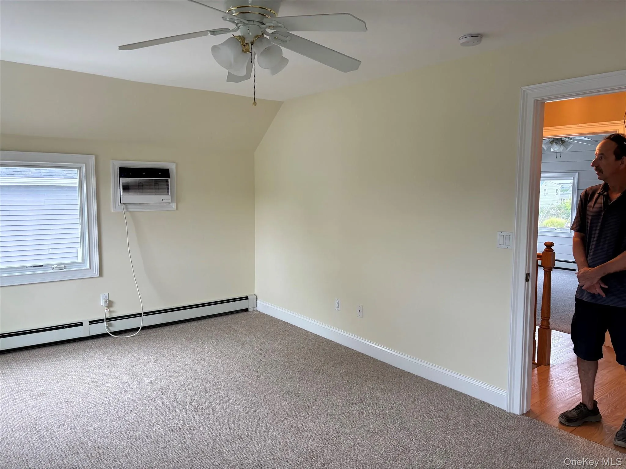 Spare room featuring light carpet, a baseboard heating unit, lofted ceiling, ceiling fan, and a wall unit AC Spare room featuring light carpet, a baseboard heating unit, lofted ceiling, ceiling fan, and a wall unit AC