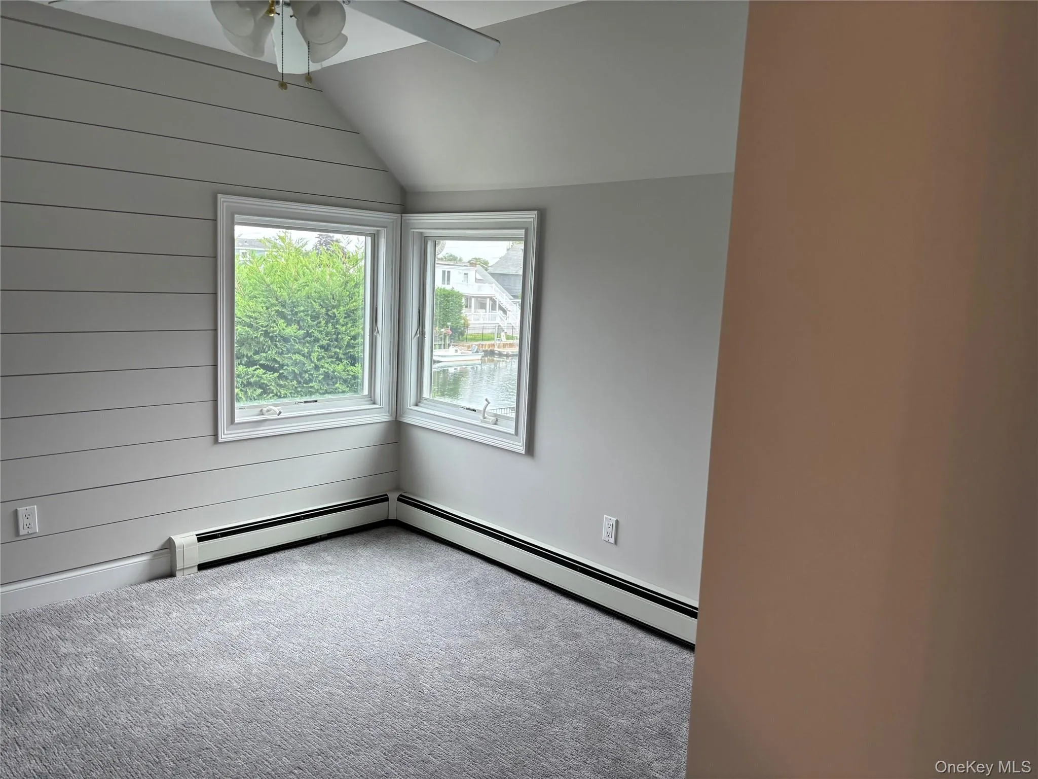 Carpeted spare room with lofted ceiling, a ceiling fan, a baseboard radiator, and wood walls Carpeted spare room with lofted ceiling, a ceiling fan, a baseboard radiator, and wood walls