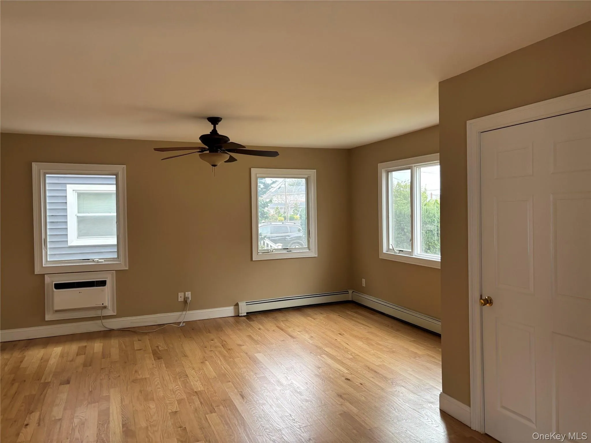 Empty room featuring plenty of natural light, light wood-type flooring, an AC wall unit, and baseboard heating Empty room featuring plenty of natural light, light wood-type flooring, an AC wall unit, and baseboard heating